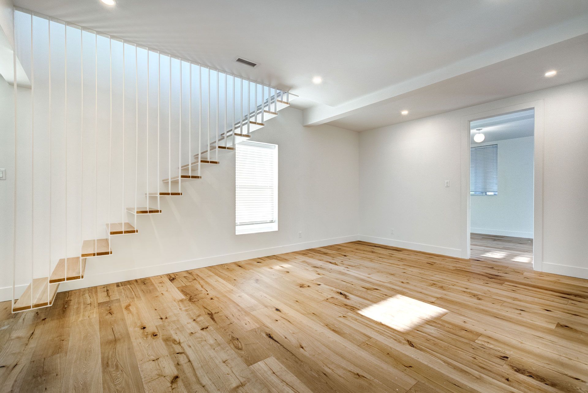 Empty room with wooden floors, white walls, floating staircase, and doorway.