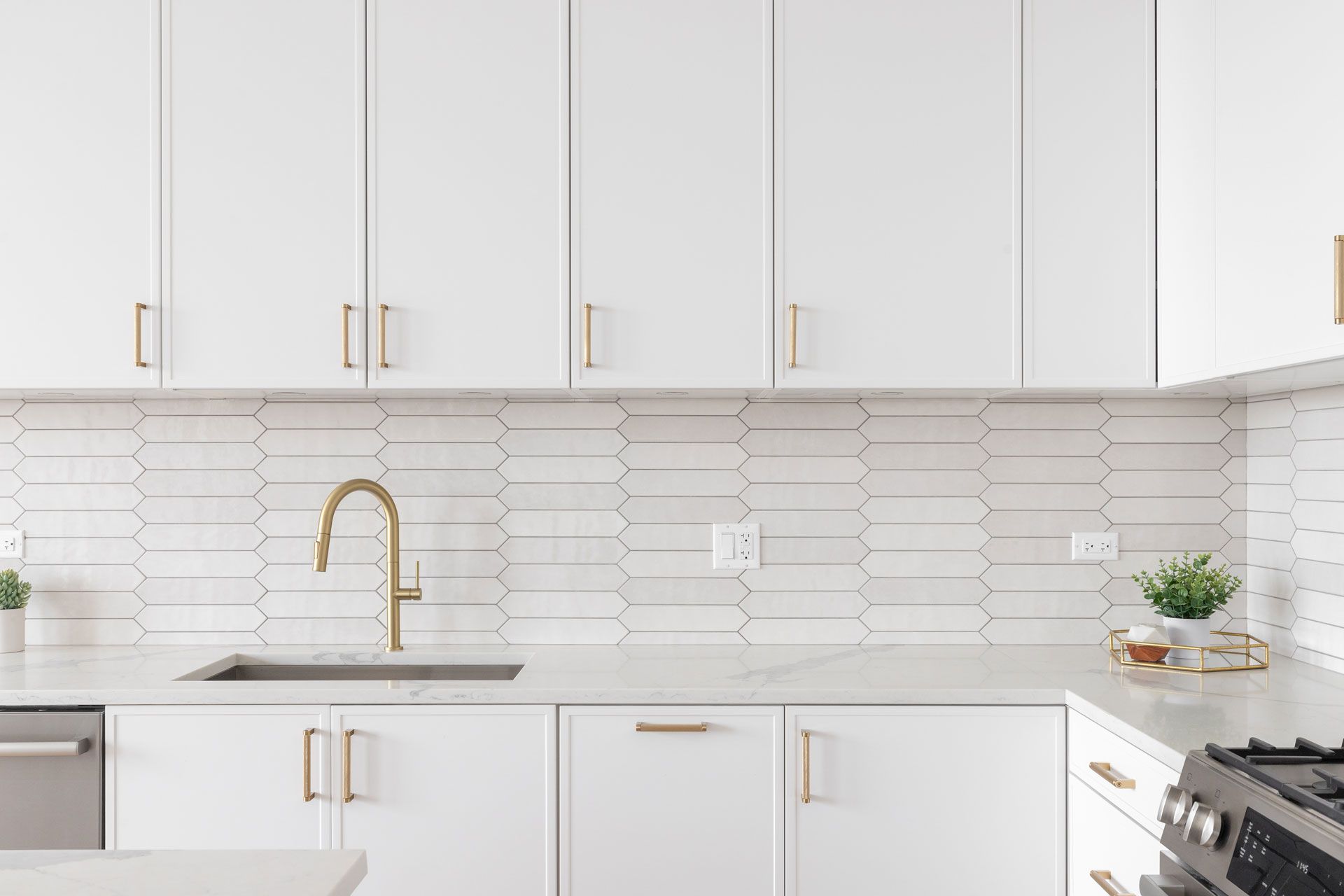White kitchen with gold fixtures, including faucet, handles, and backsplash.