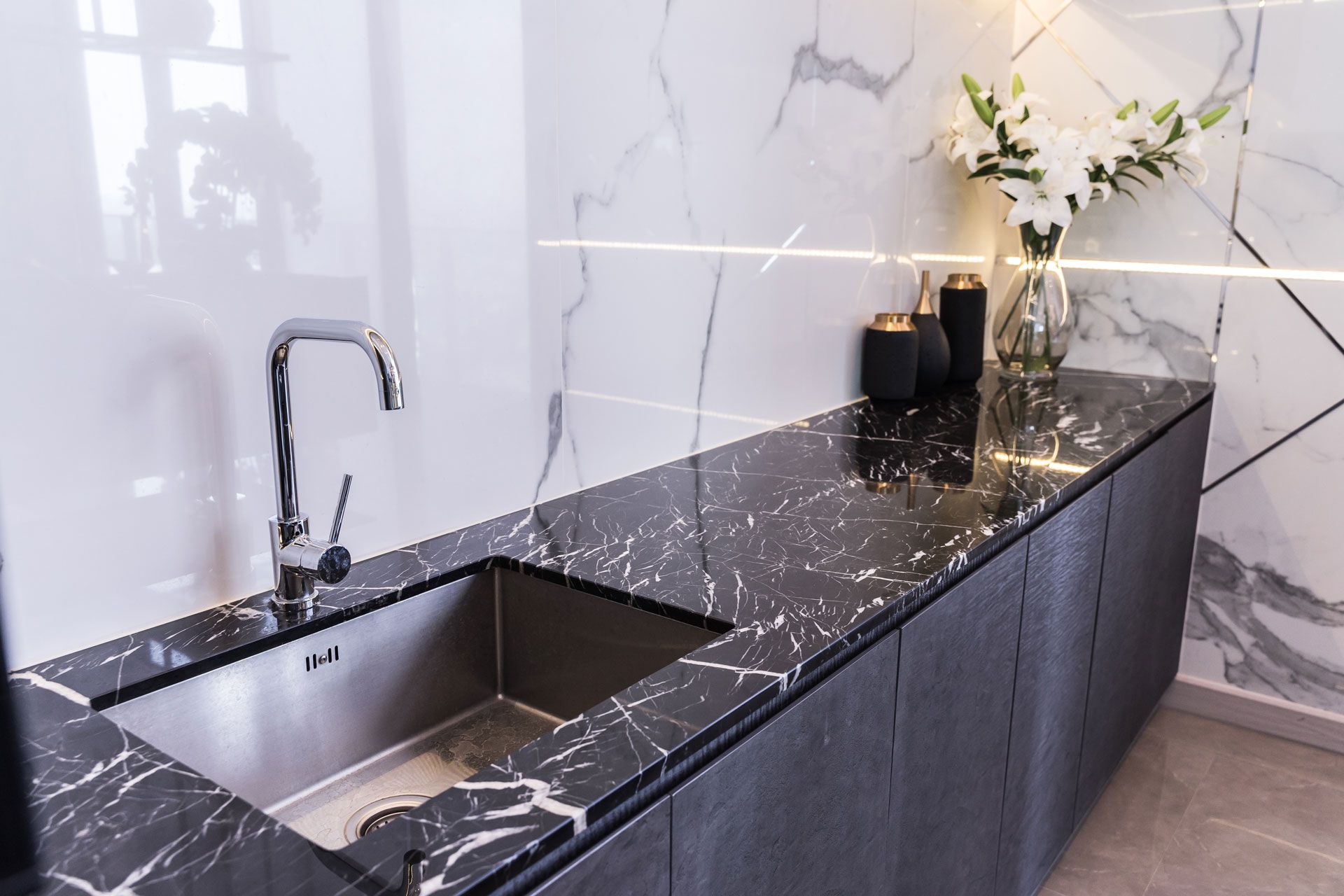 Modern kitchen with black marble countertop and sink, white floral arrangement, and marble backsplash.