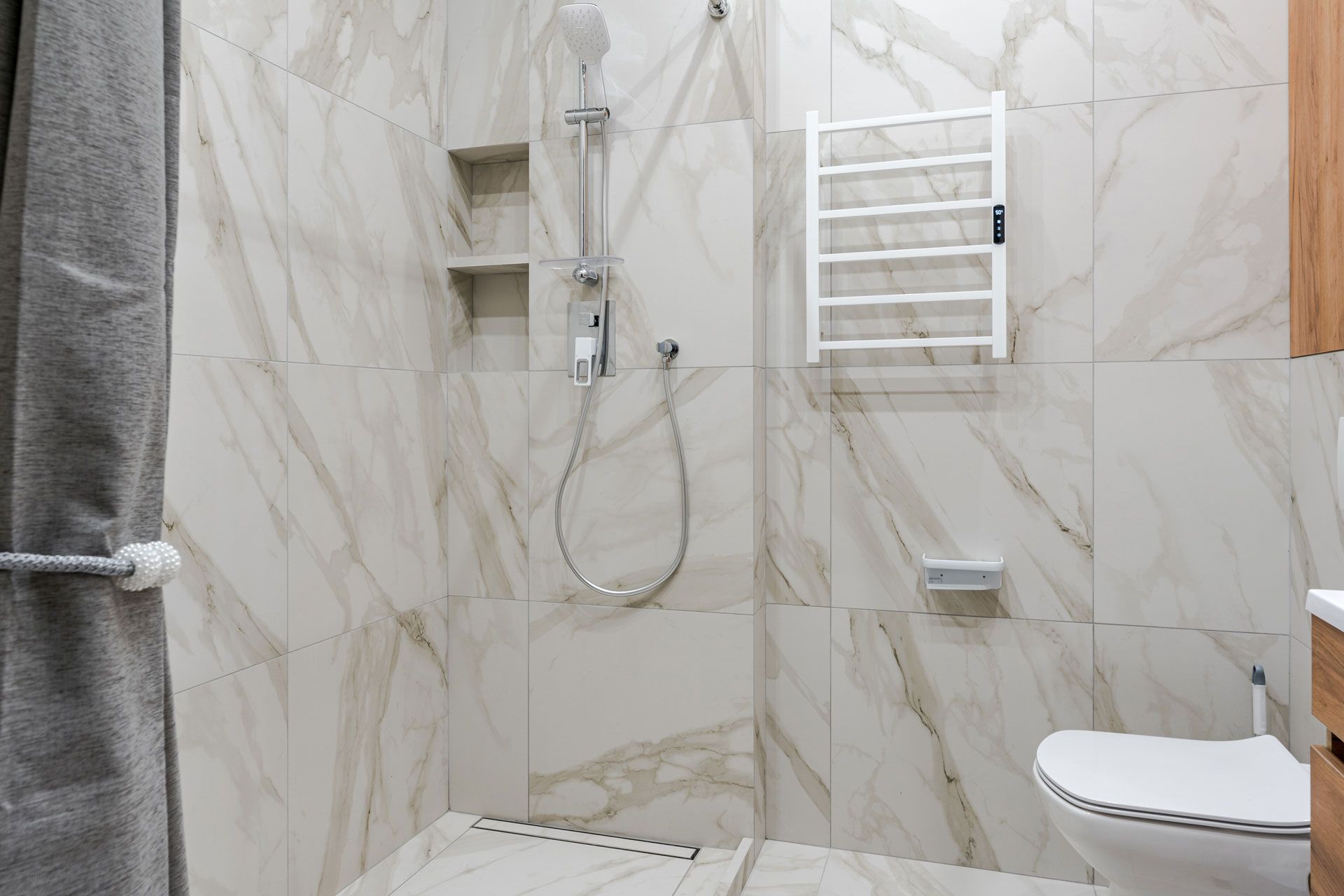 Marble-tiled shower with a rainfall showerhead, towel warmer, toilet, and gray curtain.