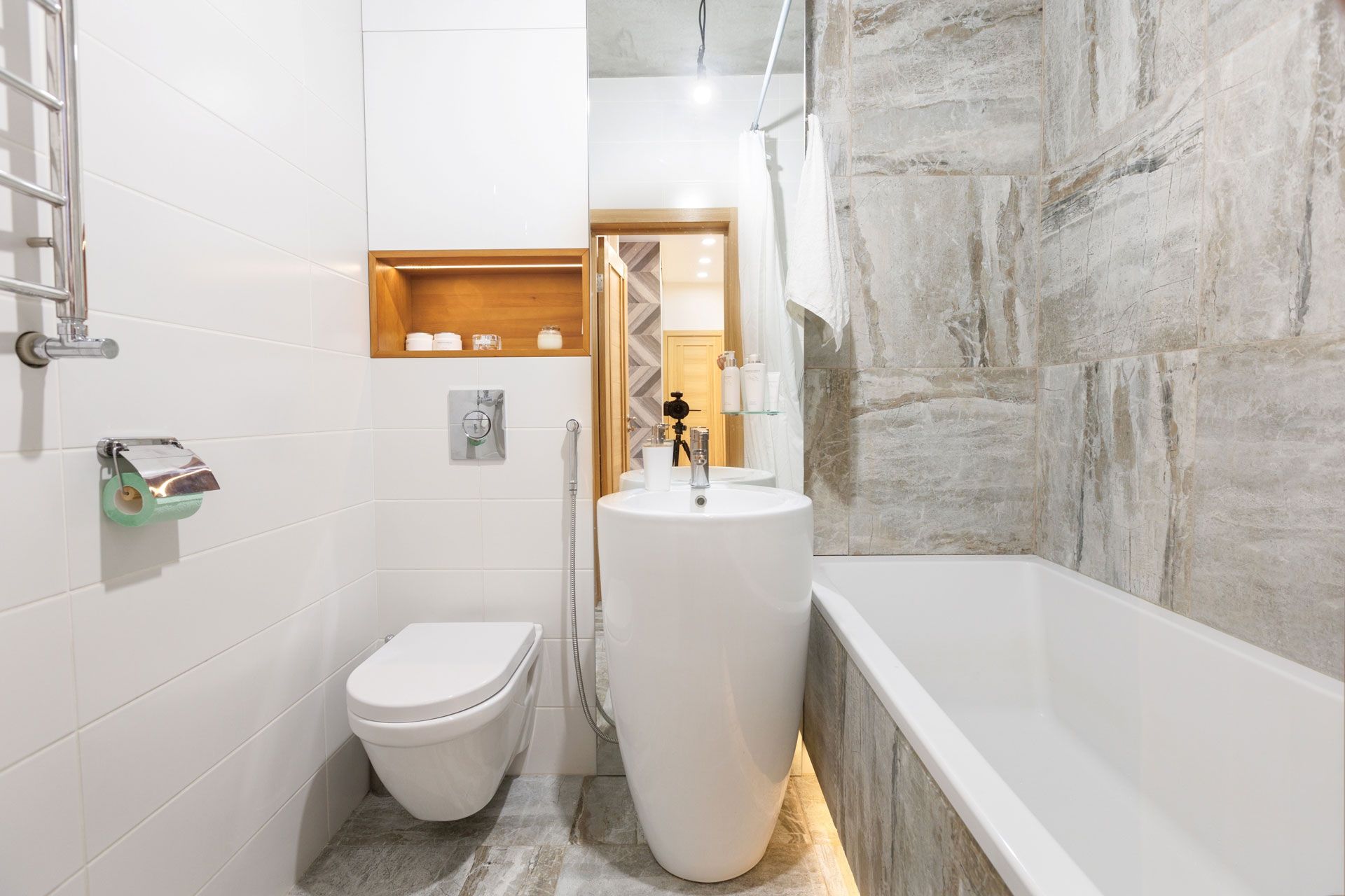 Small modern bathroom with a white pedestal sink, toilet, and bathtub. Stone wall tiles.