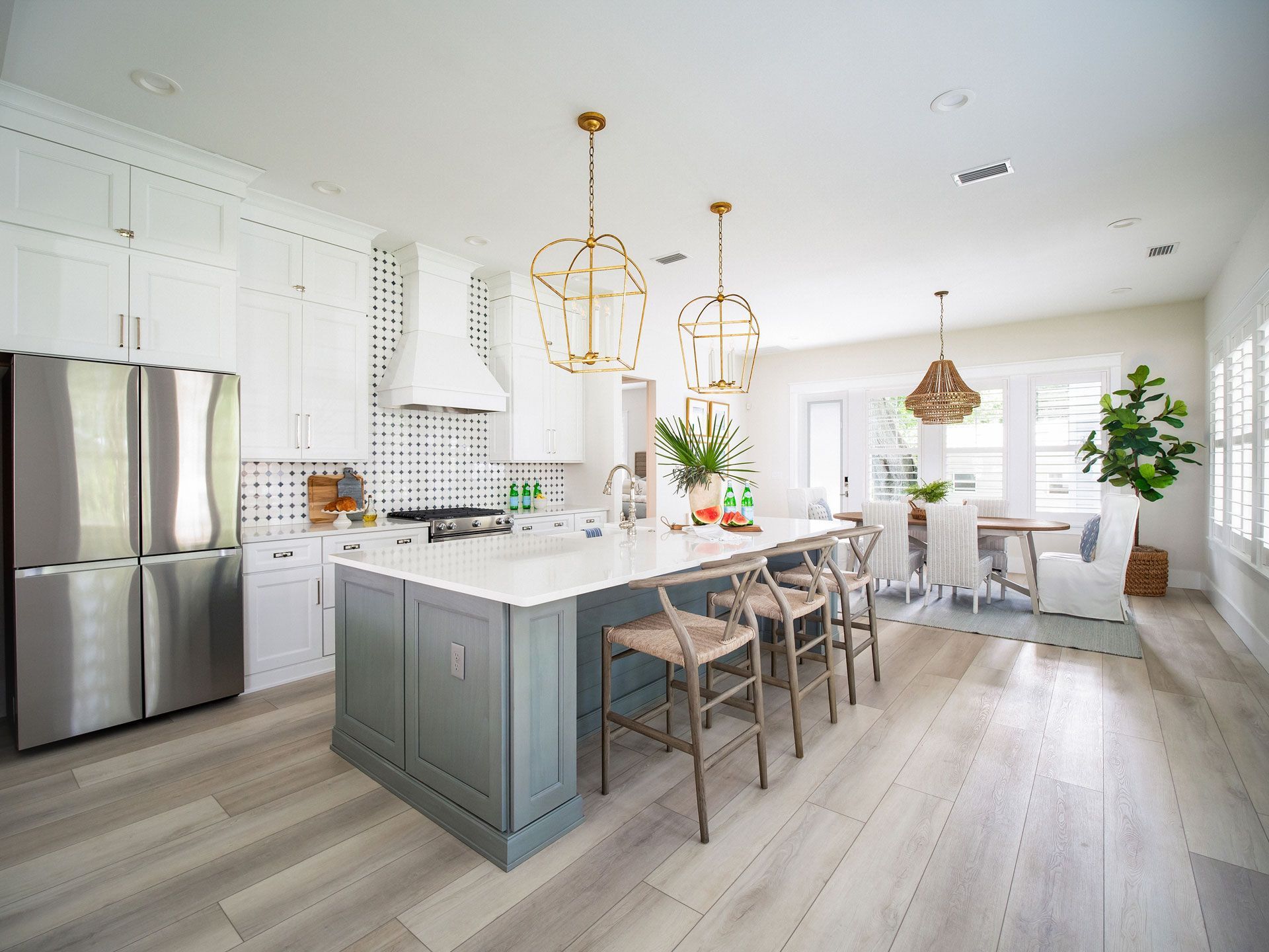 Modern kitchen with white cabinets, gray island, gold pendant lights, and light wood flooring.