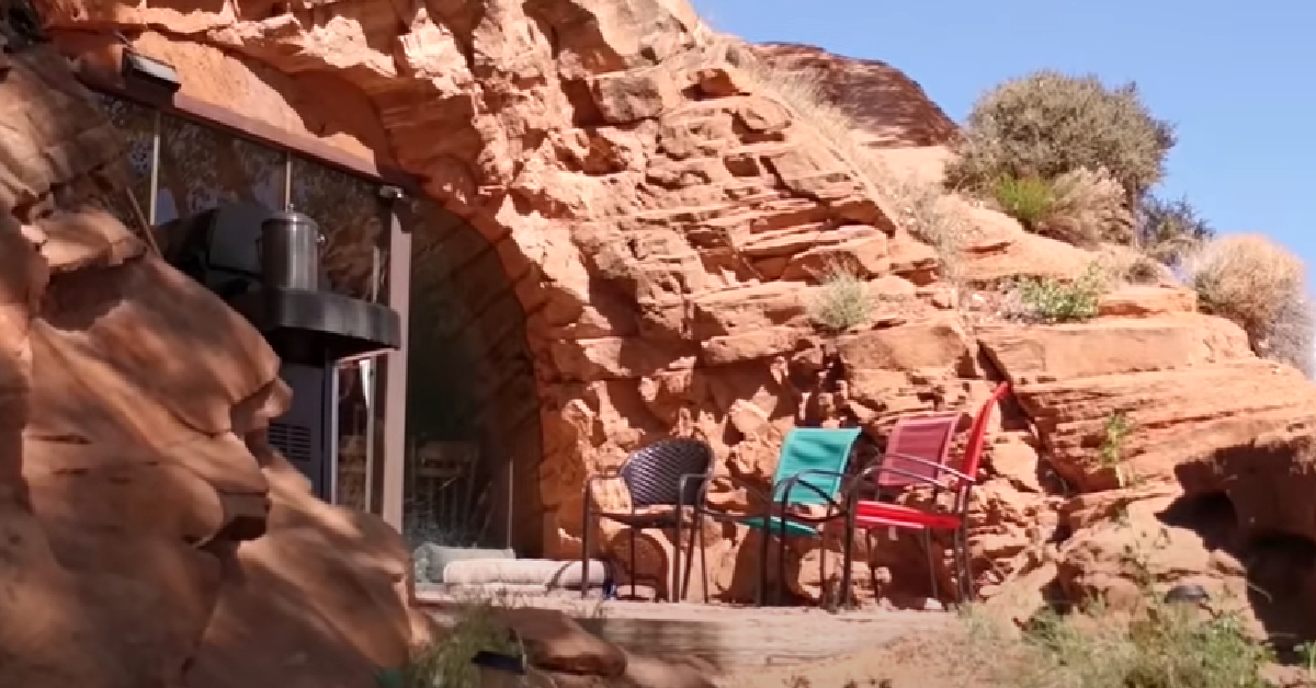 Building nestled in red rock cliff with chairs on a patio.