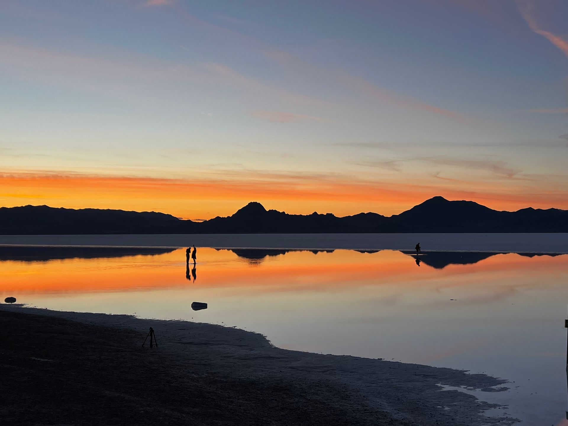 Sunset over calm lake, silhouetted mountains in background. Reflections of orange and blue.