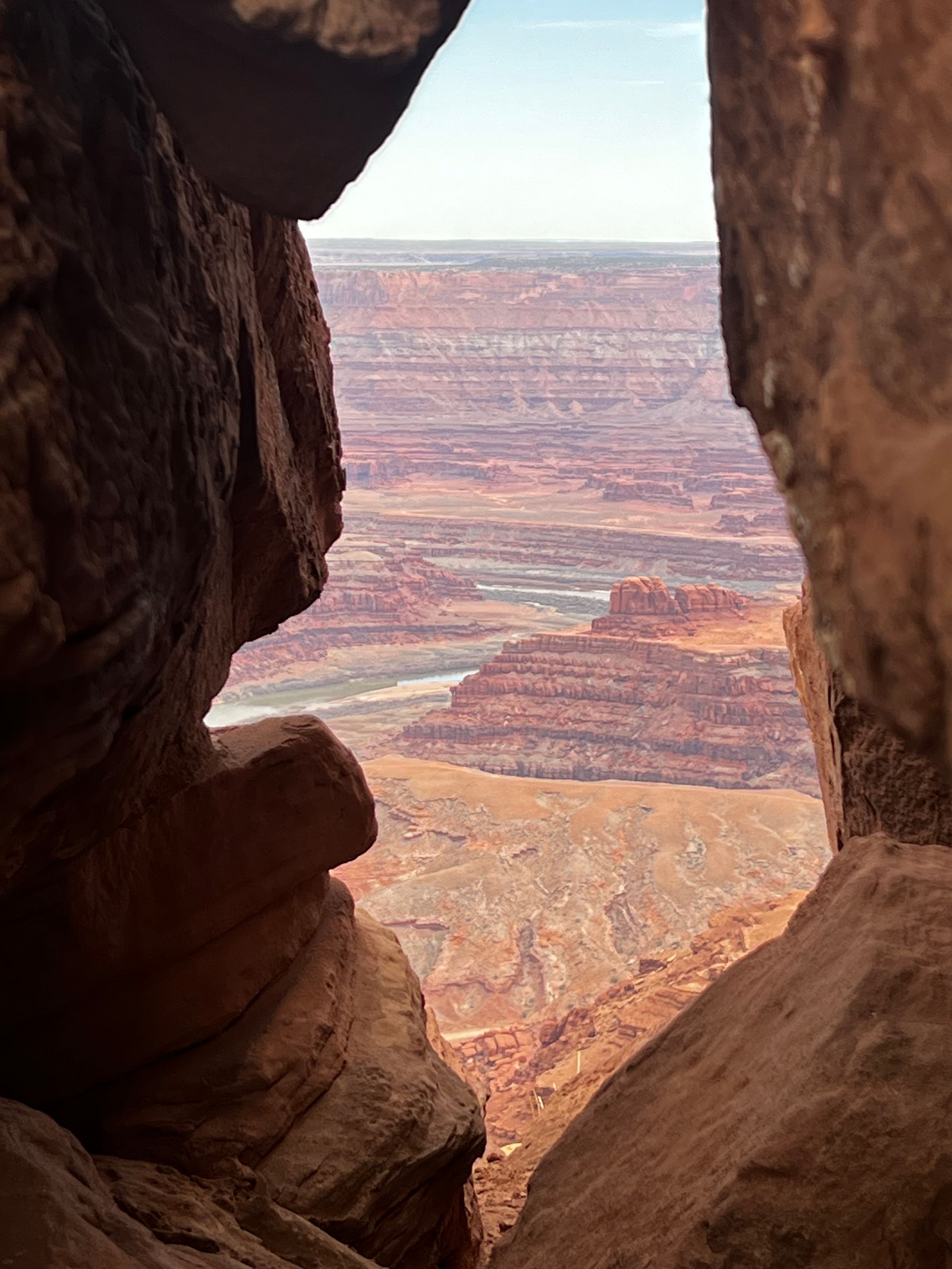 View of canyon landscape through a rock opening; red rock formations, river below.