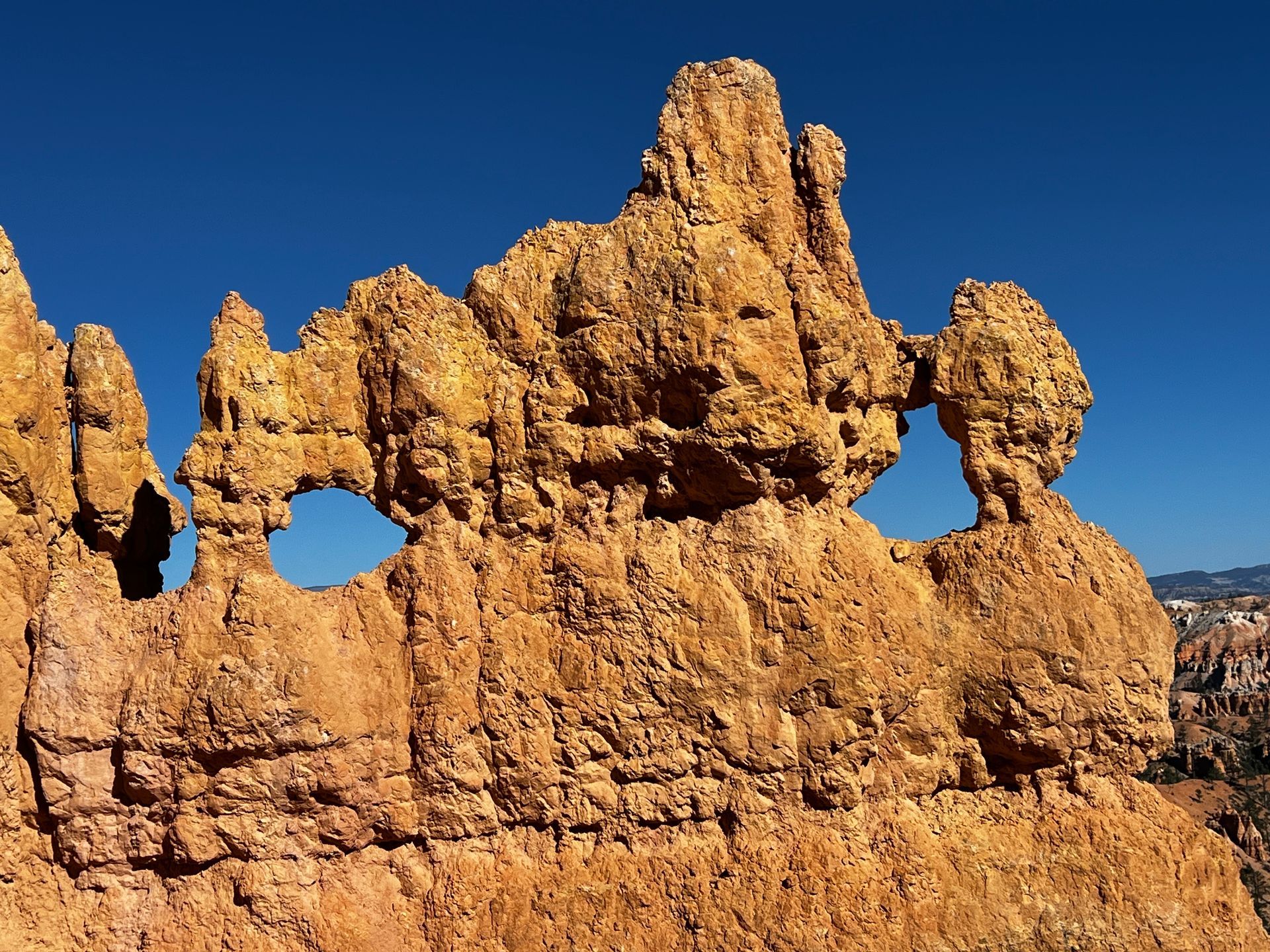 Orange rock formation with archways against a clear blue sky.