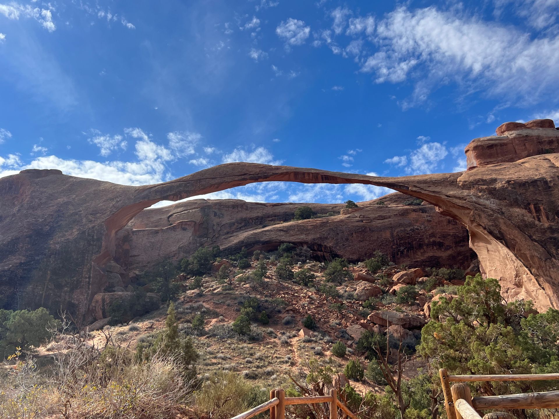 Landscape Arch in Arches National Park, Utah; sandstone arch spans across canyon, blue sky with clouds.