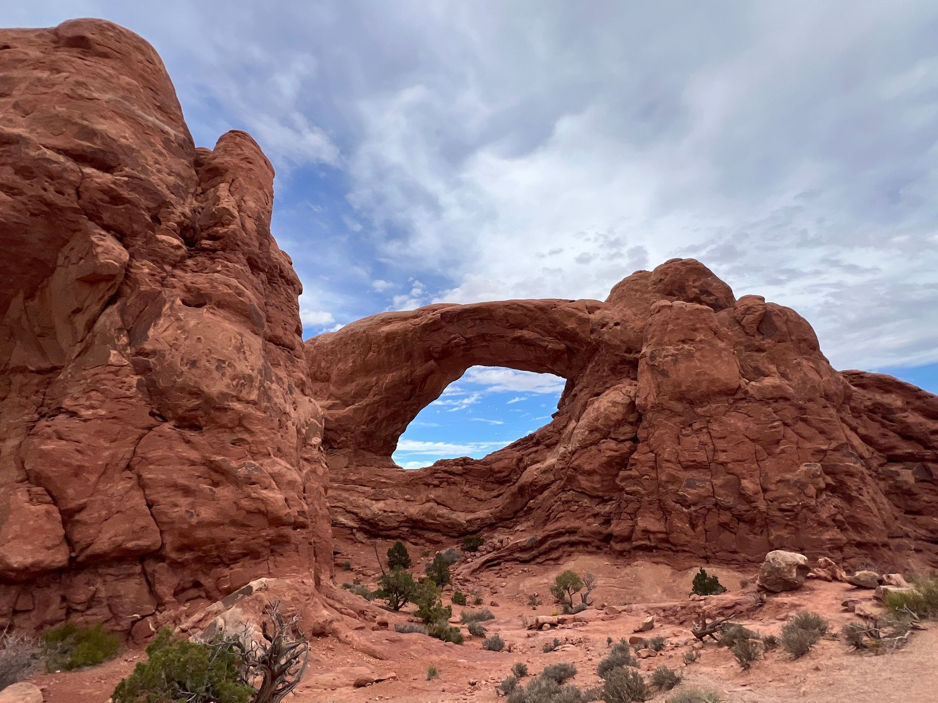 Red sandstone arch in a desert landscape under a partly cloudy blue sky.