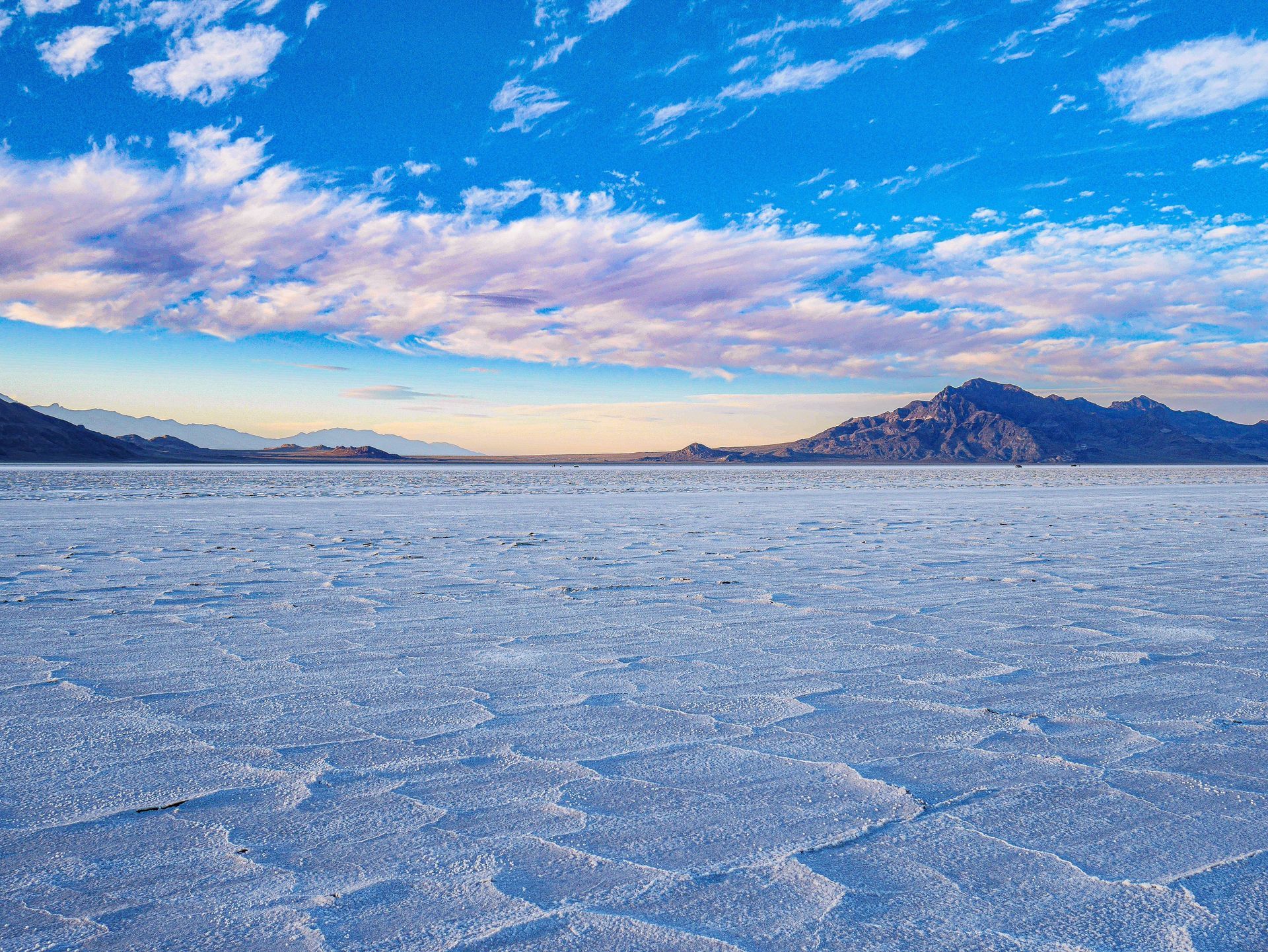 Vast white salt flats under a blue sky with scattered clouds and distant mountains.