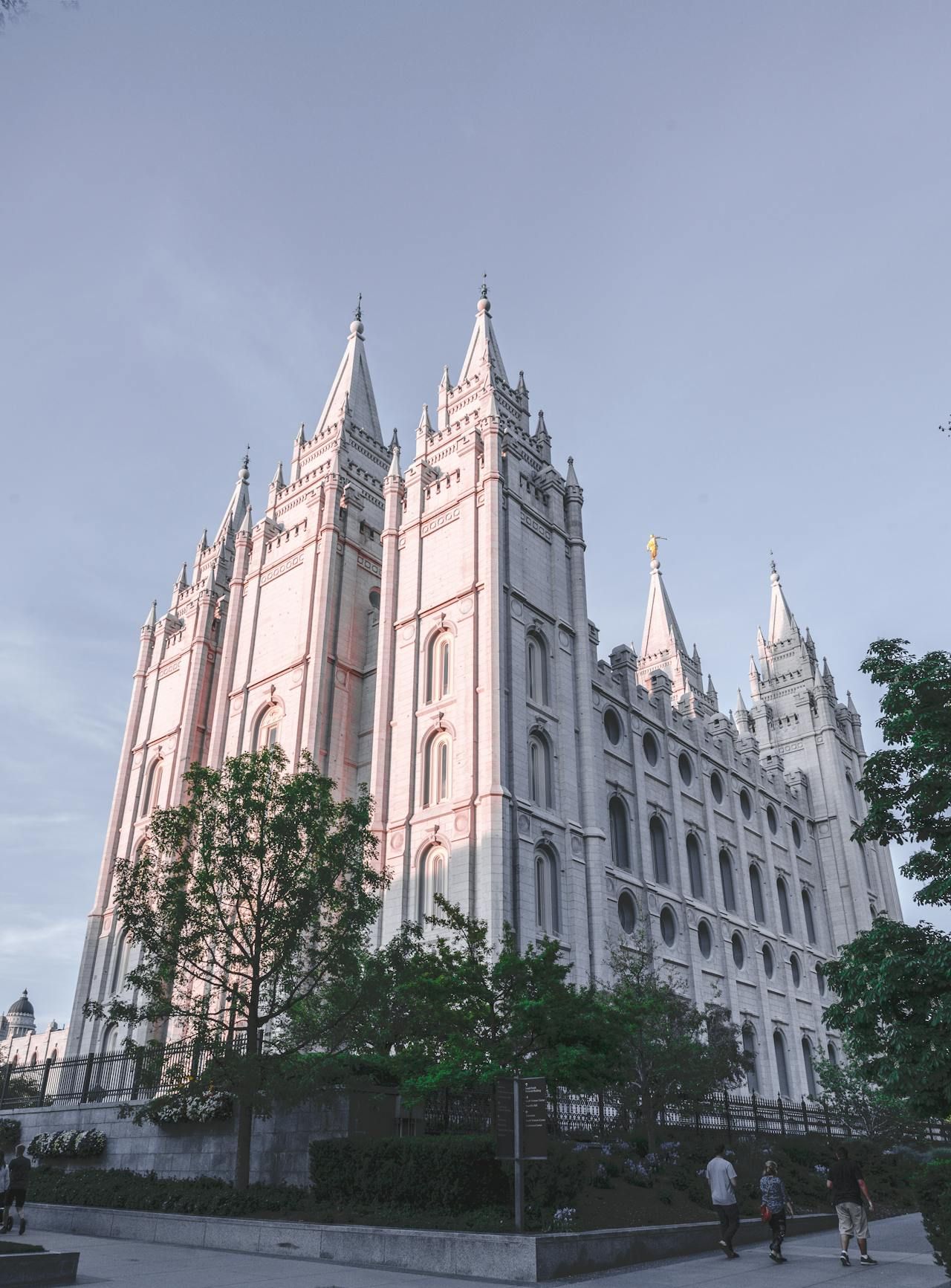 Salt Lake Temple, a large white building with spires against a blue sky, trees in foreground.