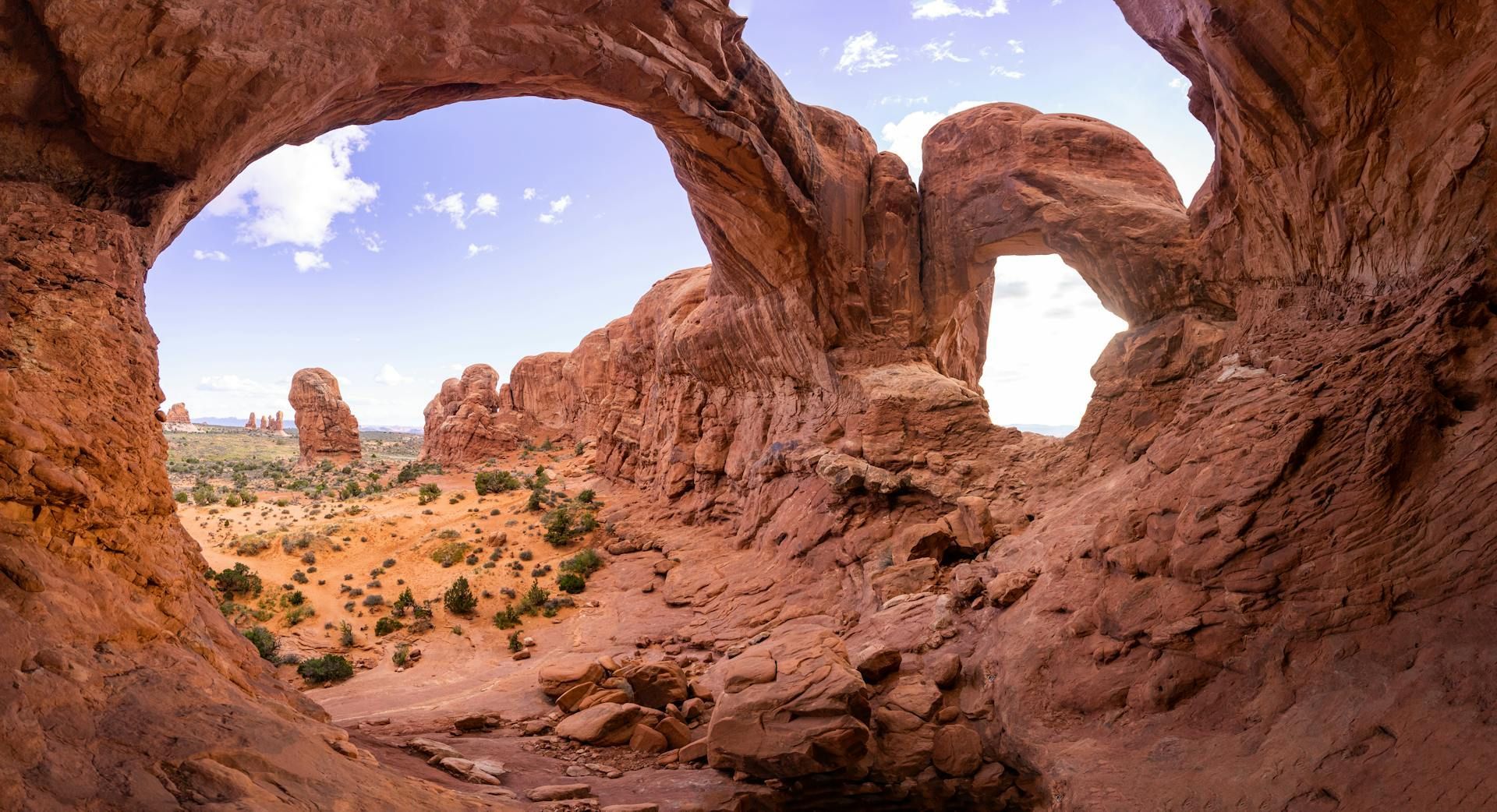 Red rock arches in a desert landscape with blue sky and scattered clouds.