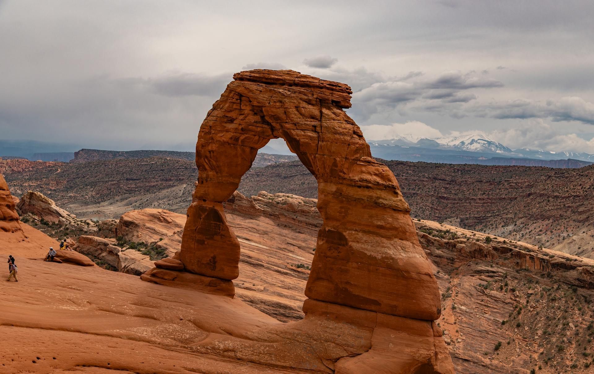 Delicate Arch in Arches National Park, Utah; red rock formation with snow-capped mountains in background.