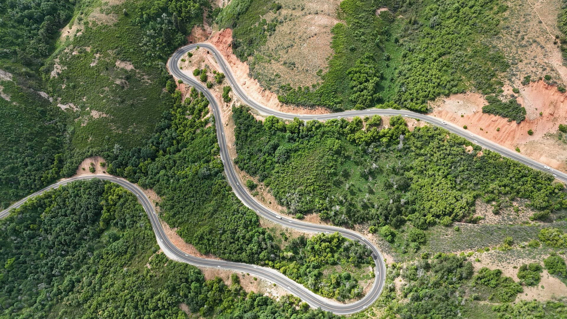 Aerial view of a winding road through a lush green, hilly landscape.
