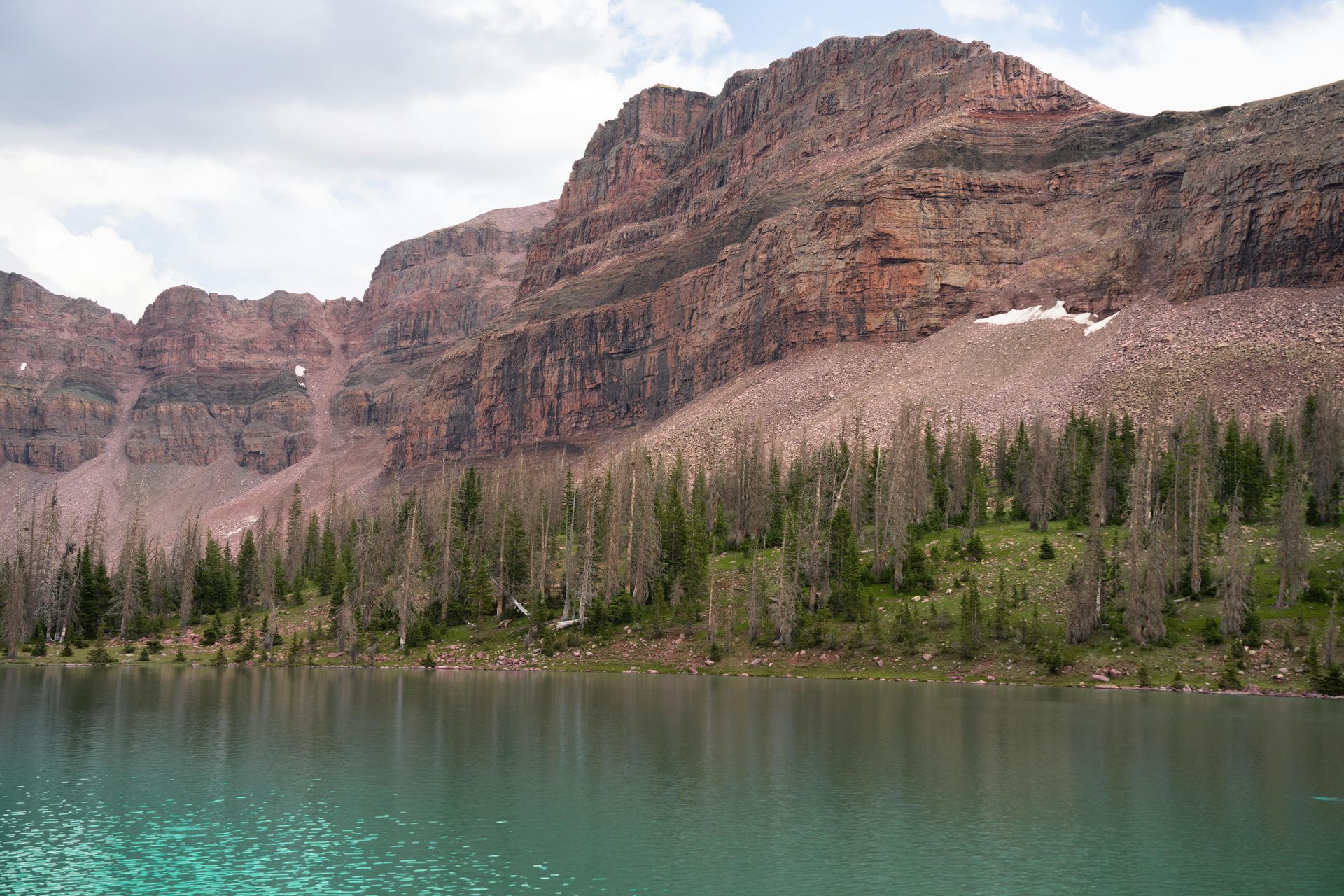Mountain range rises above a turquoise lake, with a treeline at the water's edge.