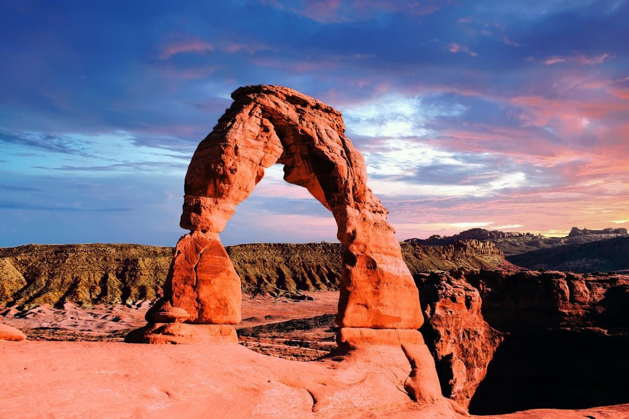 Delicate Arch in Arches National Park, Utah, silhouetted against a colorful sunset sky. Red rock formations.