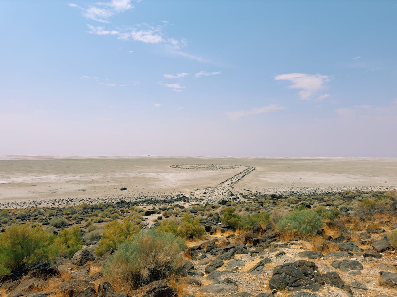 Desert landscape with sparse vegetation, gravel path, and hazy sky.
