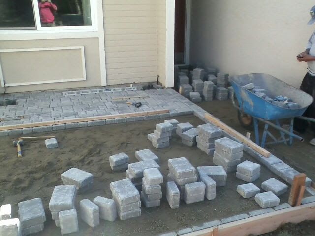 Construction site: worker laying gray paving stones in front of a house.