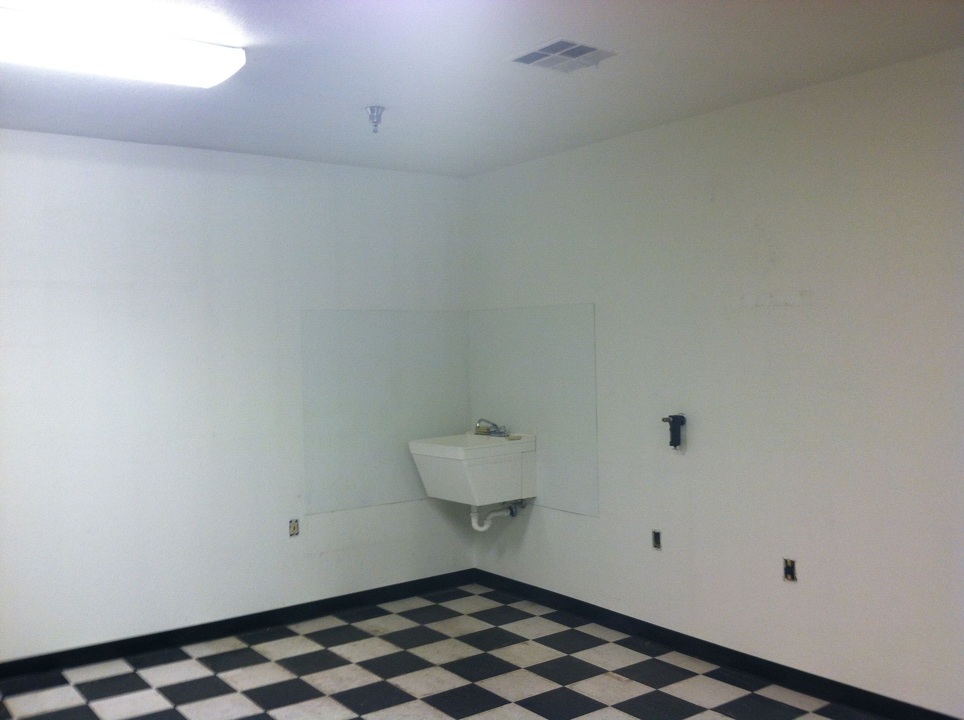Empty room with a sink in a corner, black and white checkered floor, white walls.