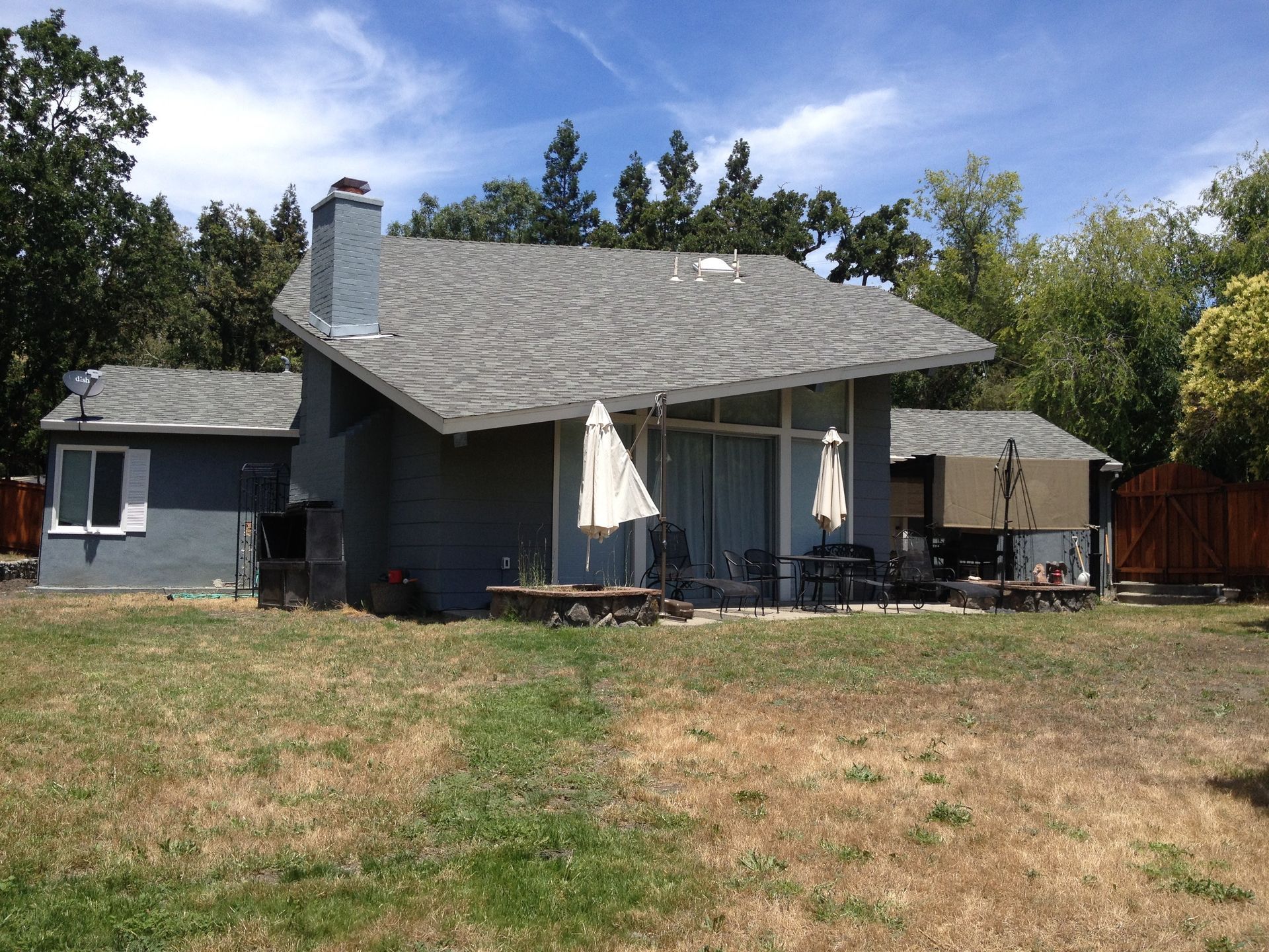 Blue house with gray roof, back patio with umbrellas, and a grassy yard.