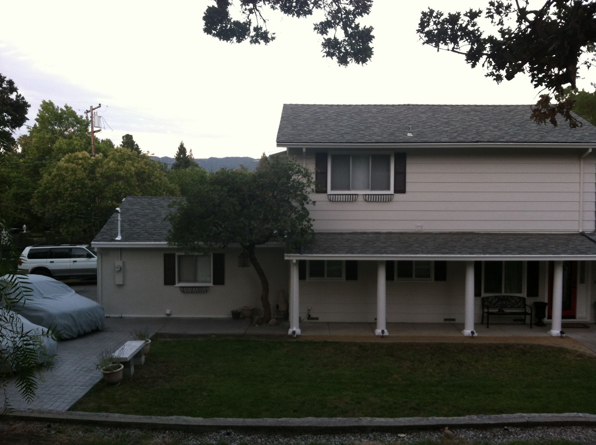 Two-story beige house with a covered porch, small yard, and a car in the driveway under a cover.