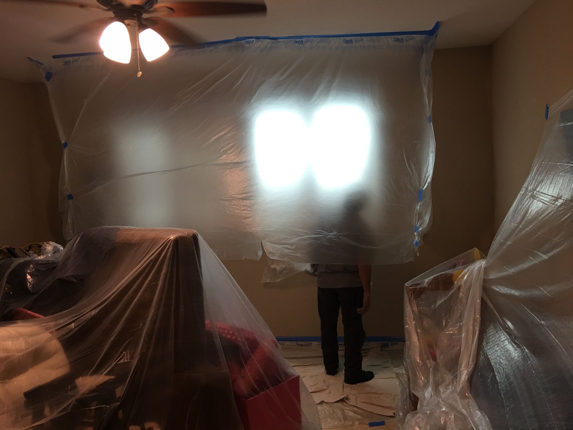 Person standing in room covered in plastic sheeting, potentially painting.