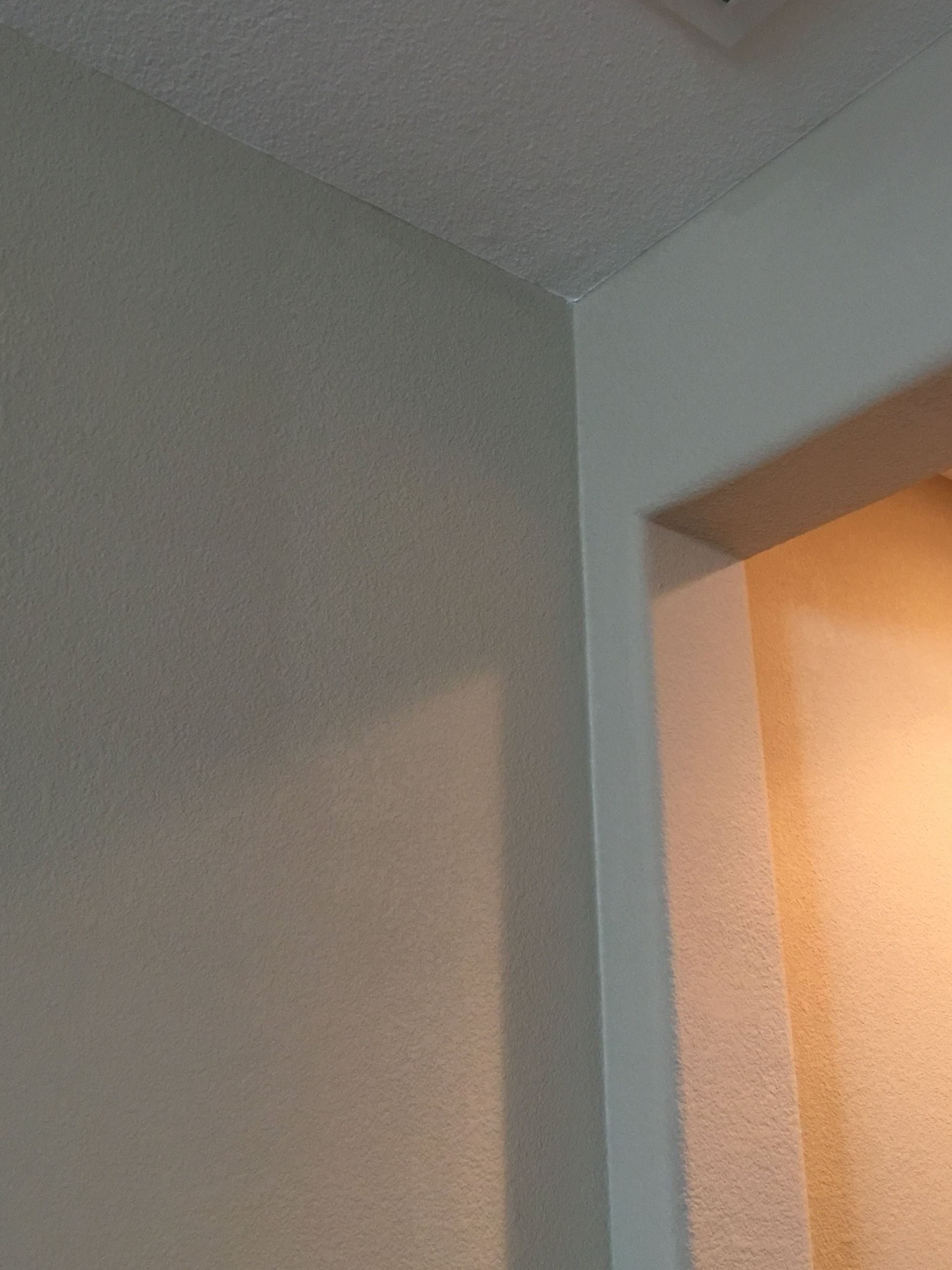 Corner of a beige textured wall meeting a white door frame. Ceiling is also textured.