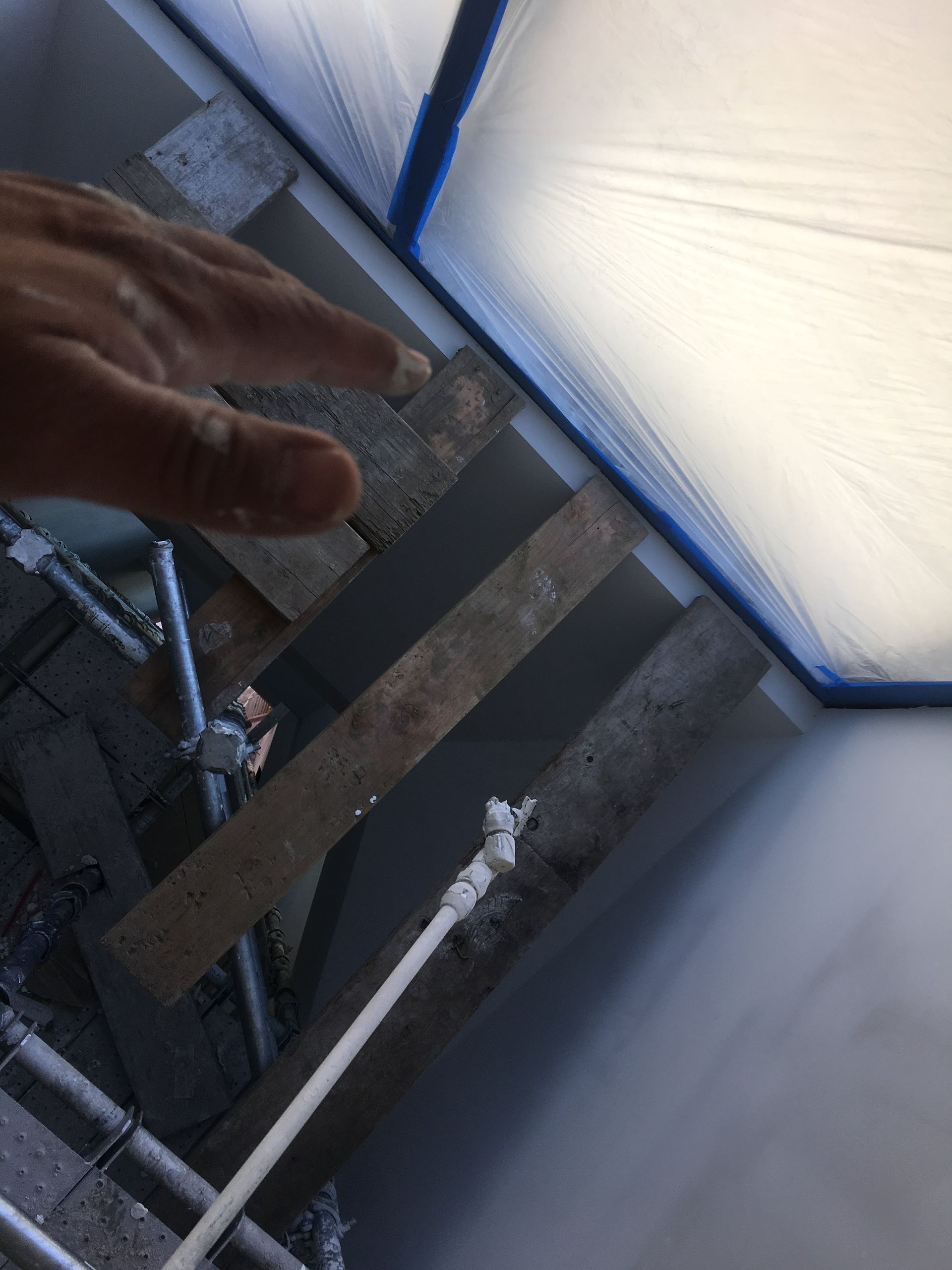 Hand pointing towards wooden planks on scaffolding, near a masked-off wall.