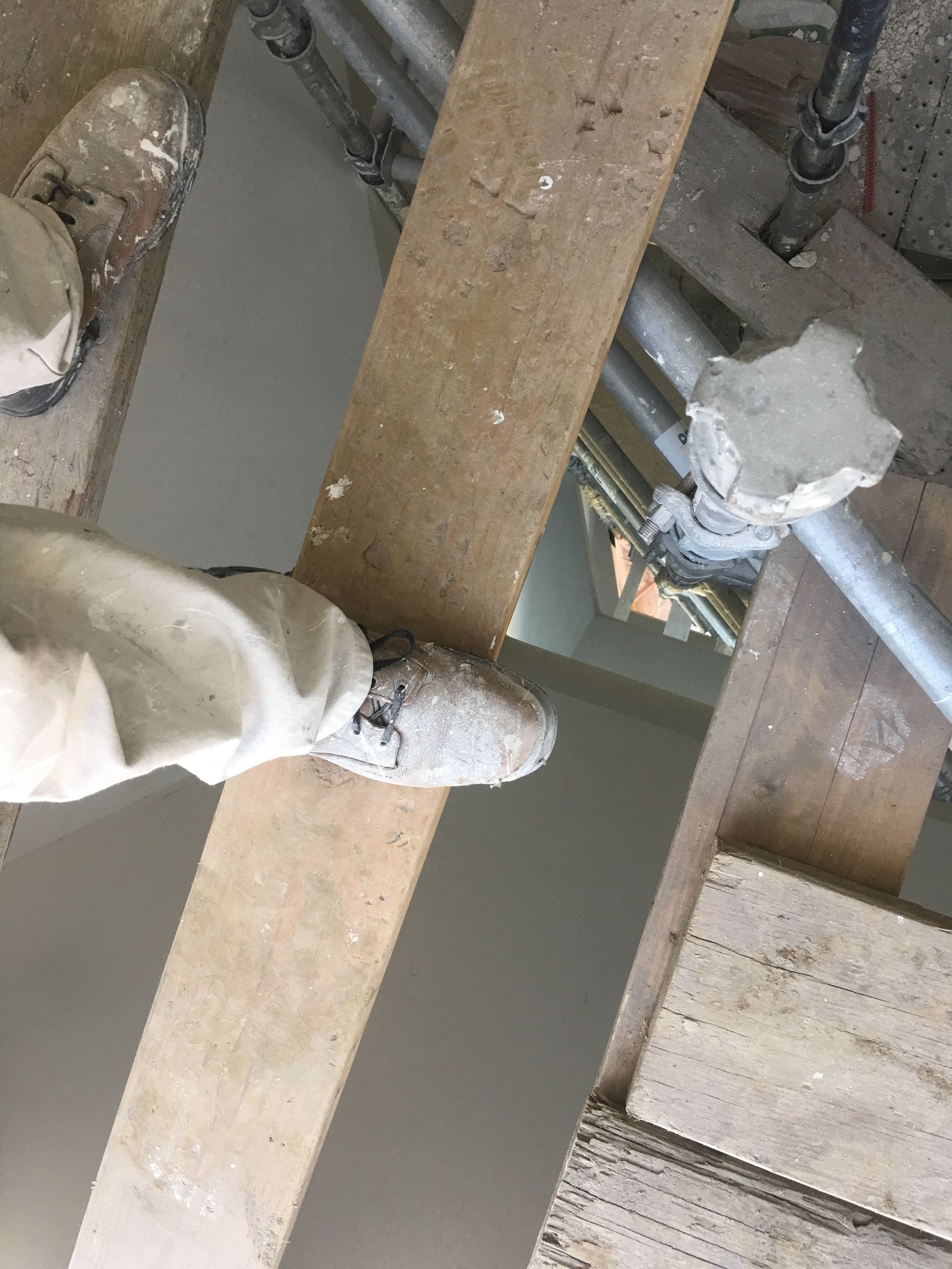 Person's feet with dirty boots standing on wooden planks; construction setting.