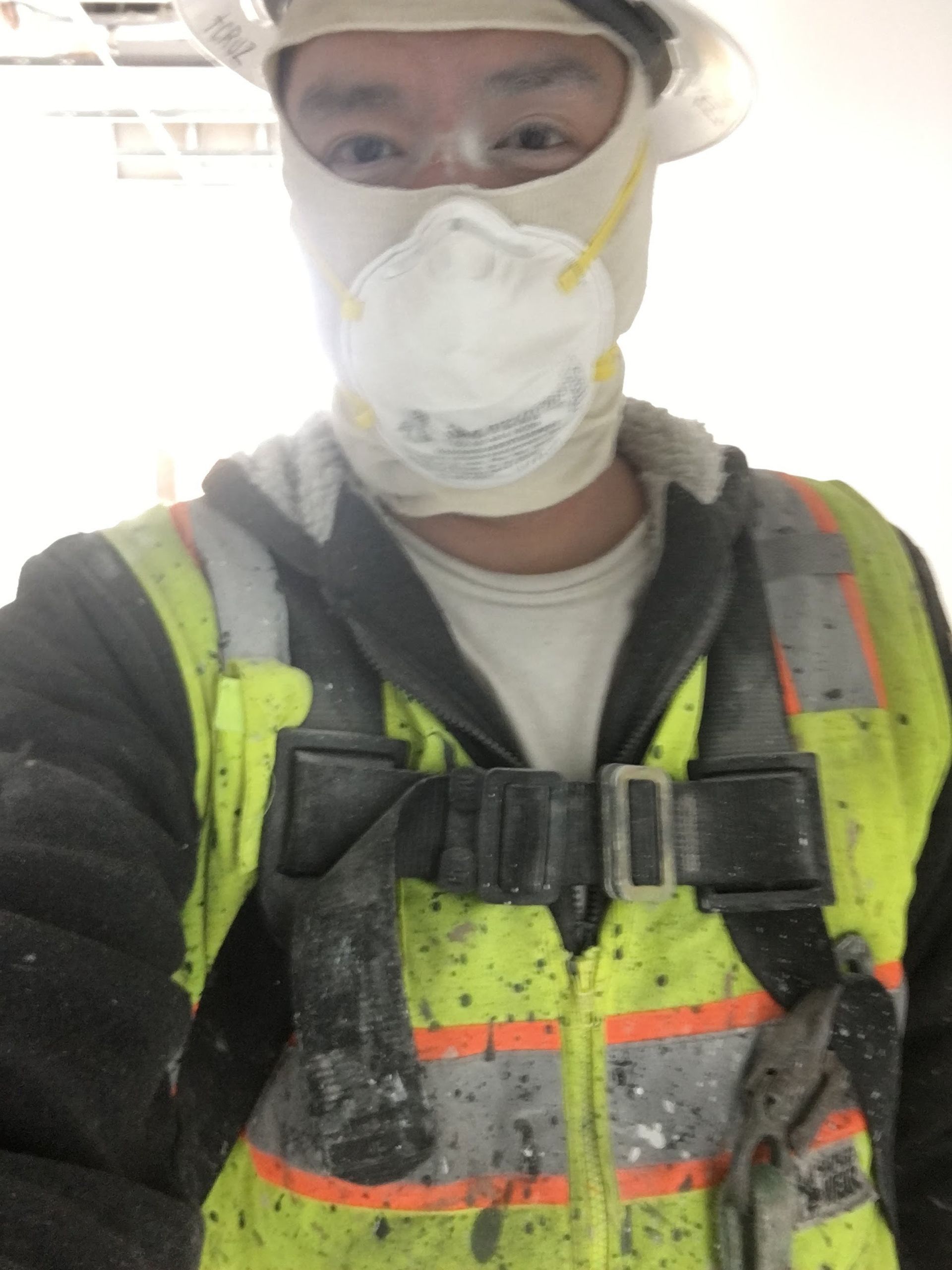 Construction worker in protective gear, face mask, and safety vest, indoors.