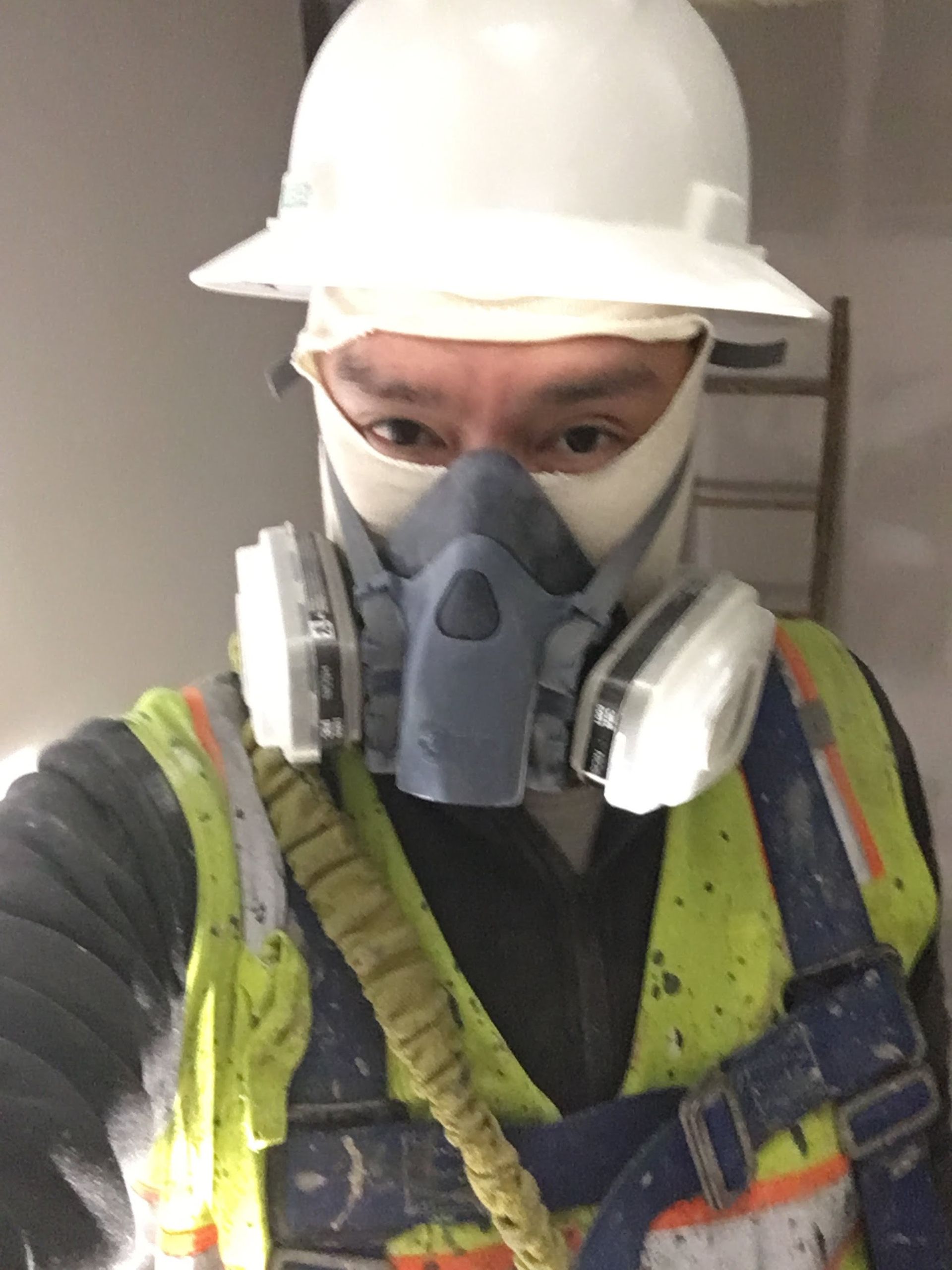 Person wearing a hard hat, respirator, and safety vest on a construction site.