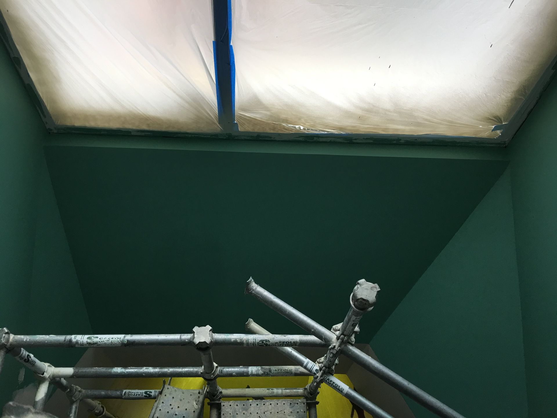 Green-painted room with scaffolding below a cloudy, translucent ceiling. Blue tape visible.