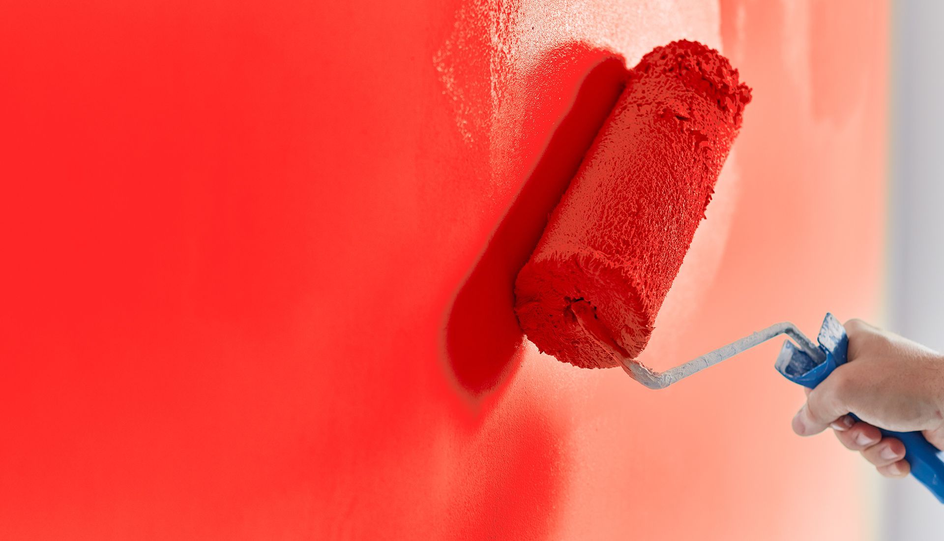 A person is painting a wall red with a paint roller.