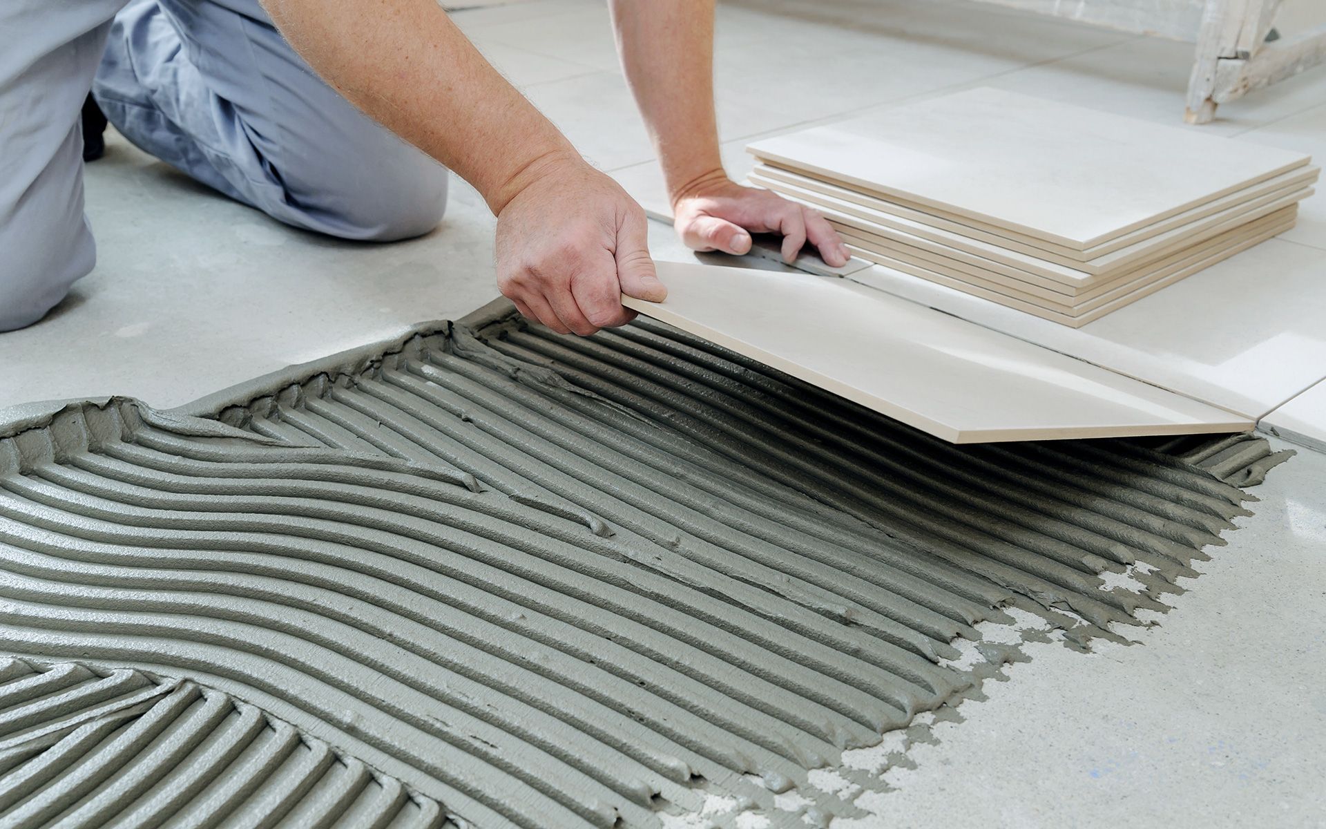 Person placing a tile on a bed of notched mortar during a tiling project.