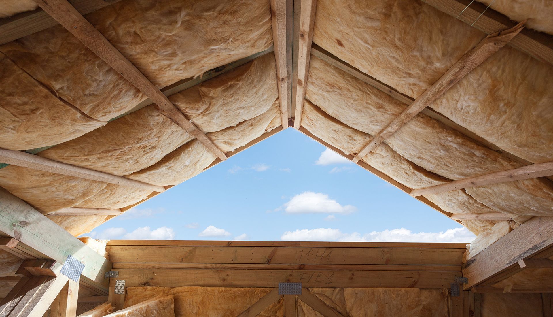 Interior view of a wooden roof under construction with insulation and a triangular opening to the sky.