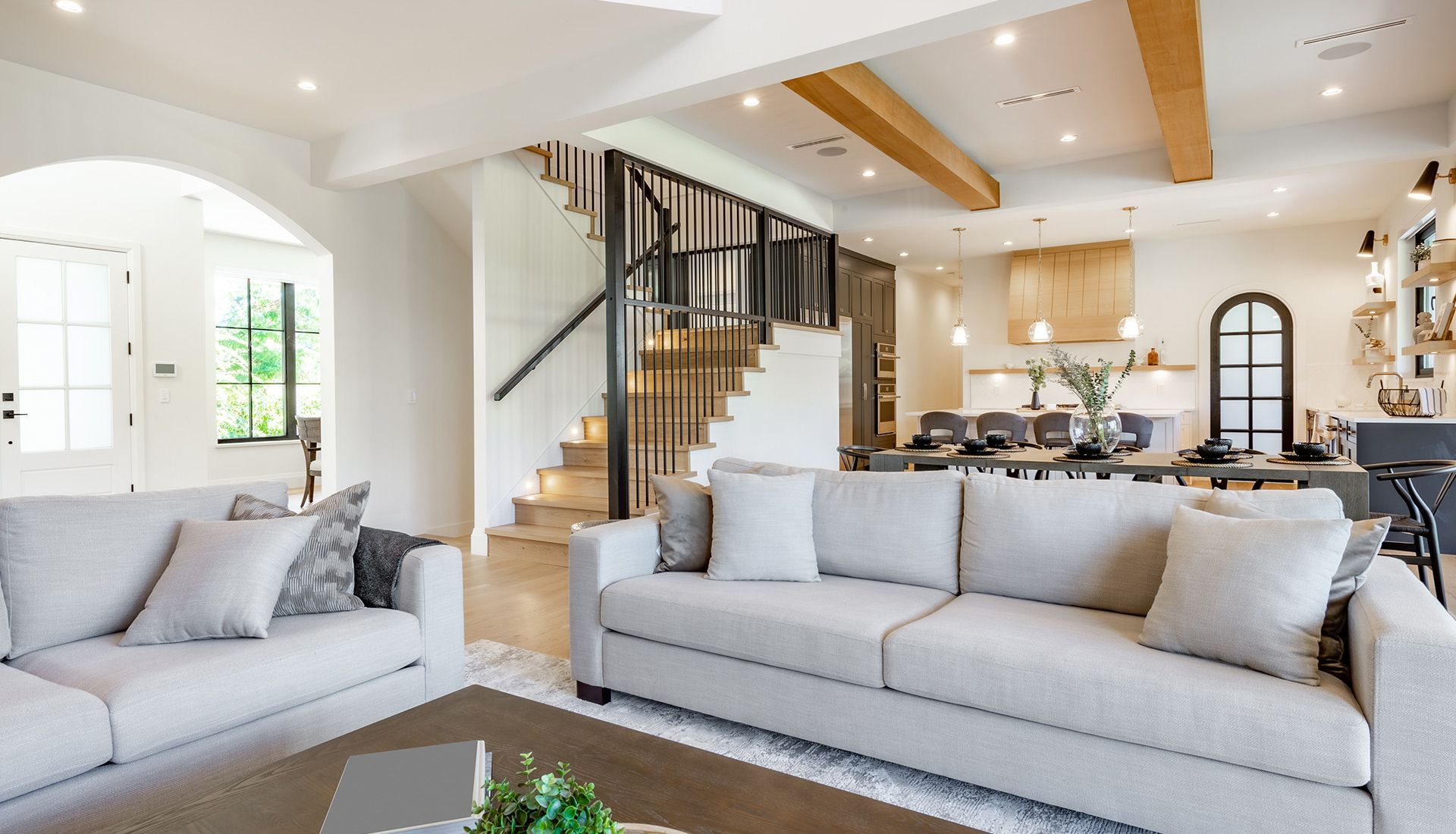 Living room with two light gray sofas, staircase, and open kitchen with dining table.