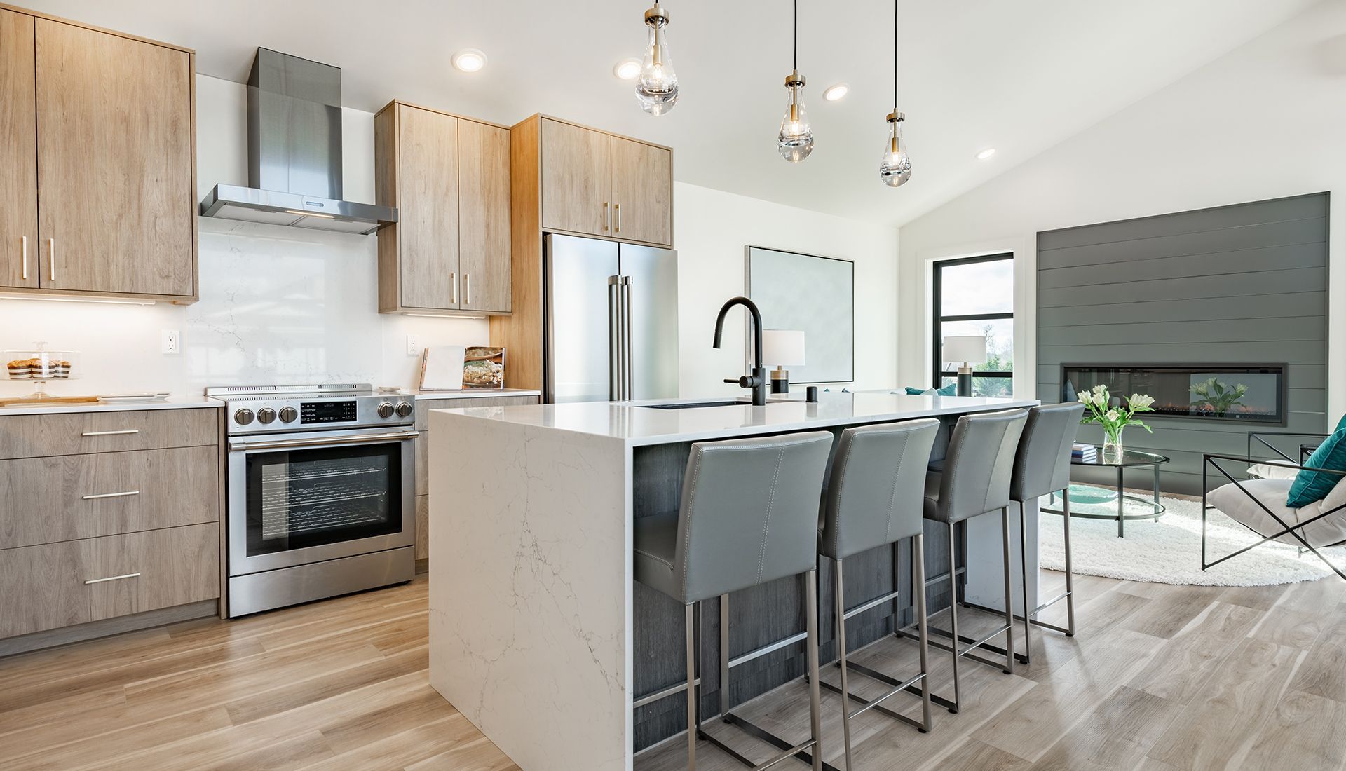 Modern kitchen with stainless steel appliances, light wood cabinets, white island with bar stools, and fireplace.