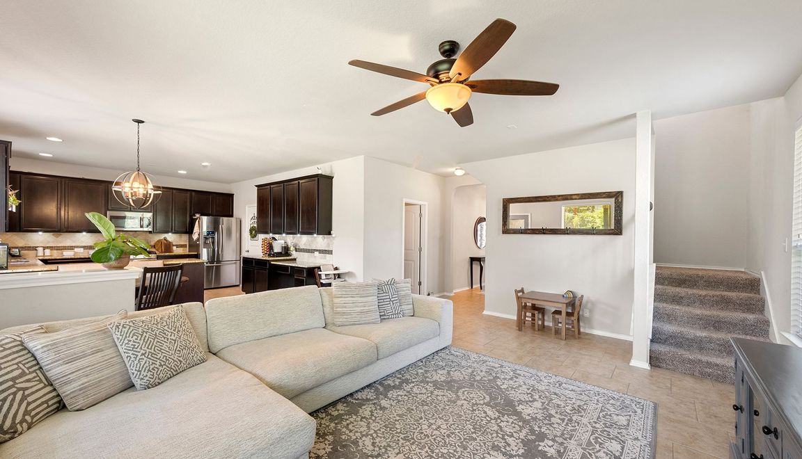 Open-concept living space with sectional sofa, kitchen, stairs, and ceiling fan.