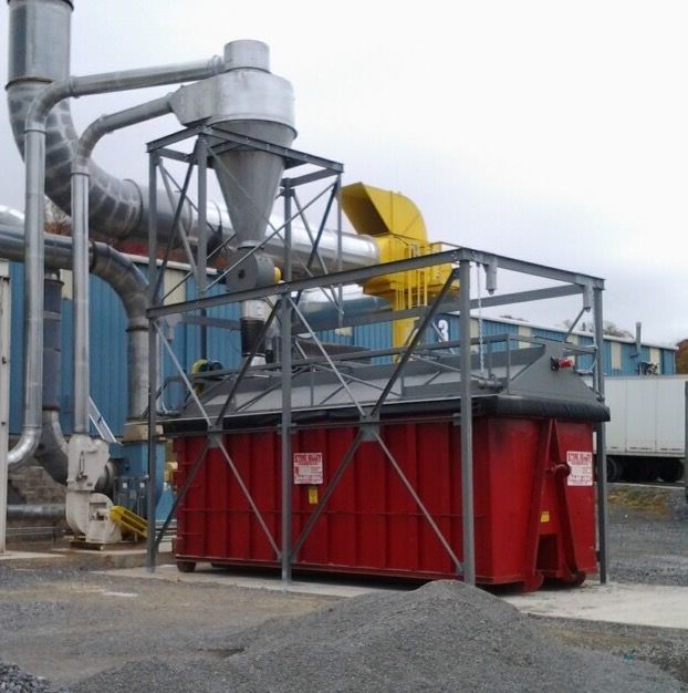A red dumpster enclosed in a metal frame, with pipes, a funnel, and debris pile.