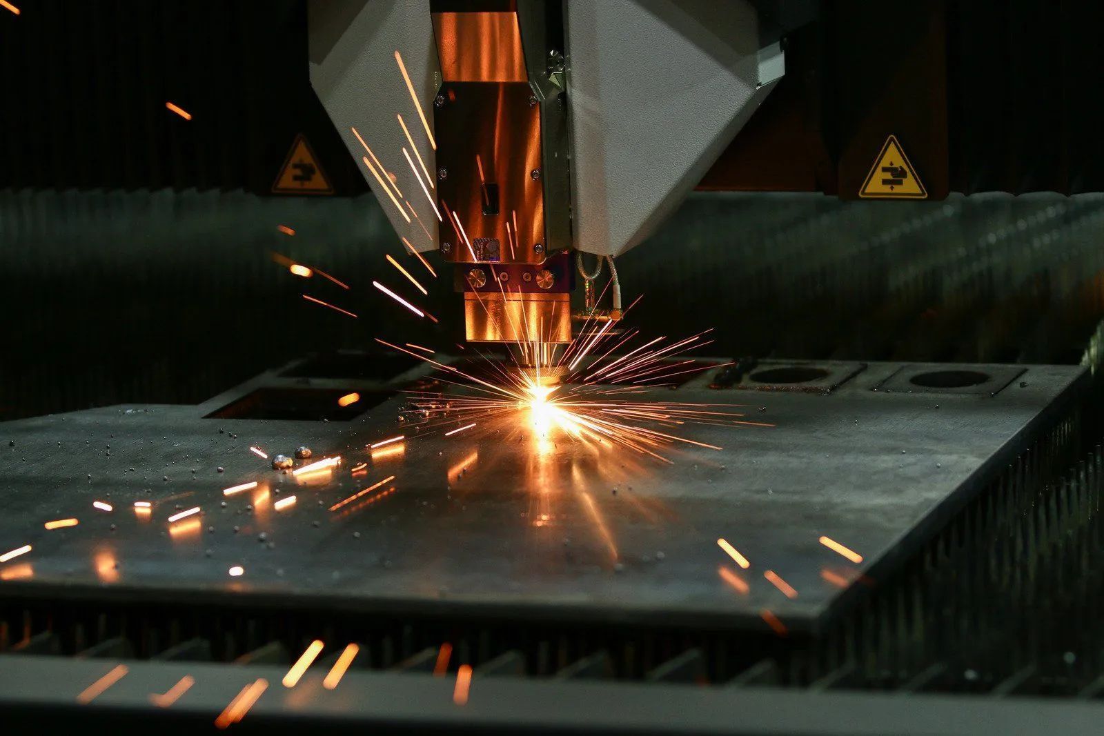 Laser cutter in action, sparks flying, cutting metal plate in an industrial setting.
