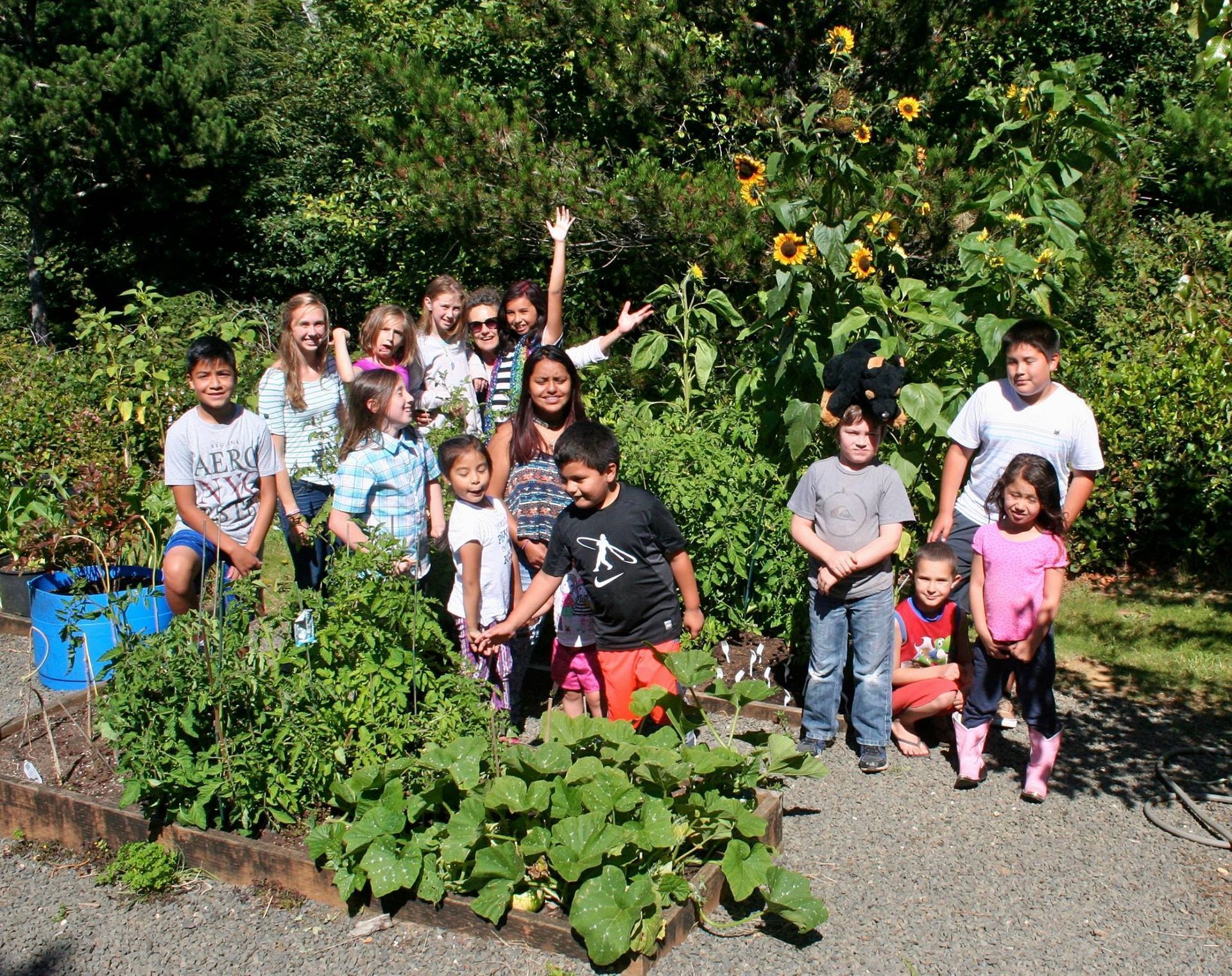 Group of children in a garden posing near plants and sunflowers; sunny day, smiles.