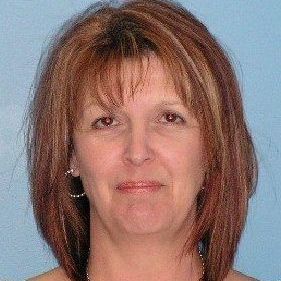 Woman with reddish-brown hair, smiling, wearing hoop earrings, against a blue backdrop.