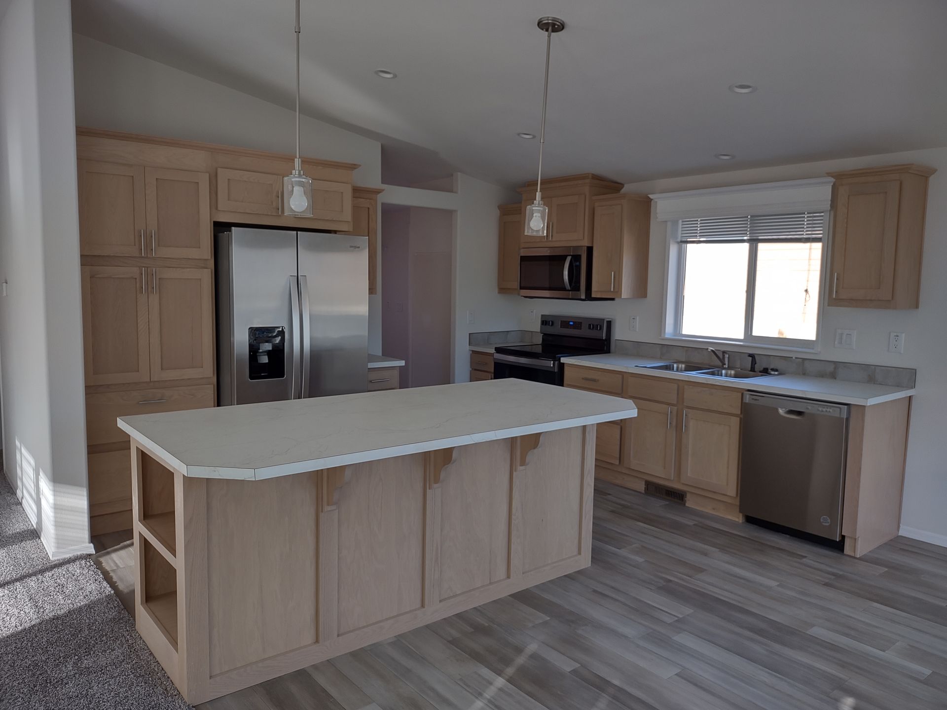 Light-wood kitchen with island, stainless steel appliances, and a window.