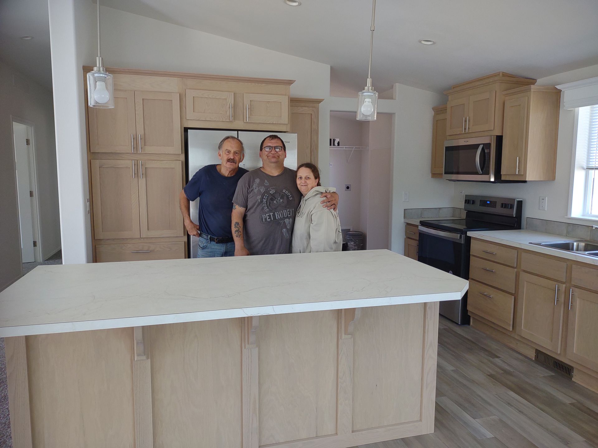 Three people stand in a new kitchen with light cabinets and island.