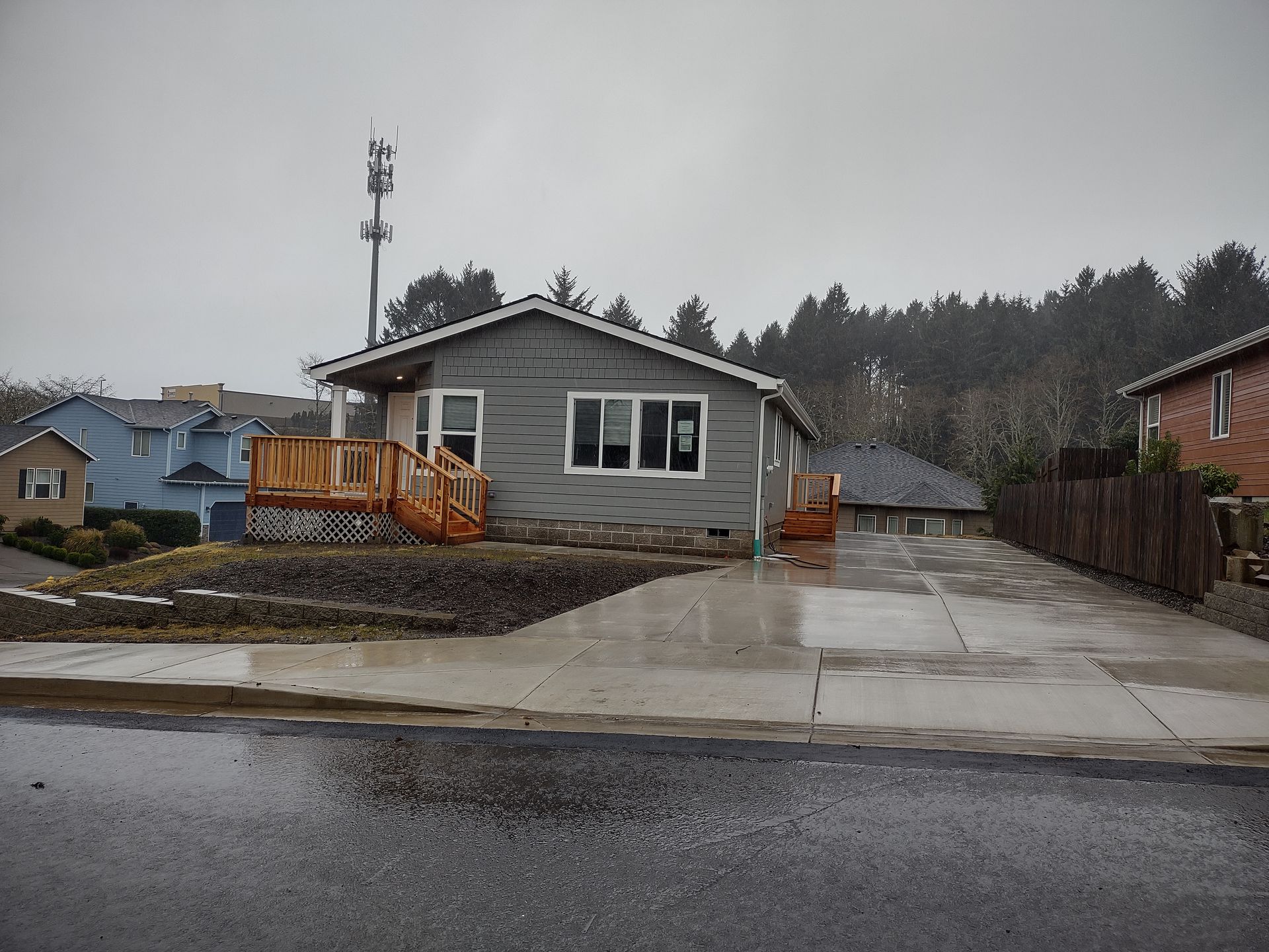 Construction site with gravel piles, orange safety poles, and a small, gray house in the background.