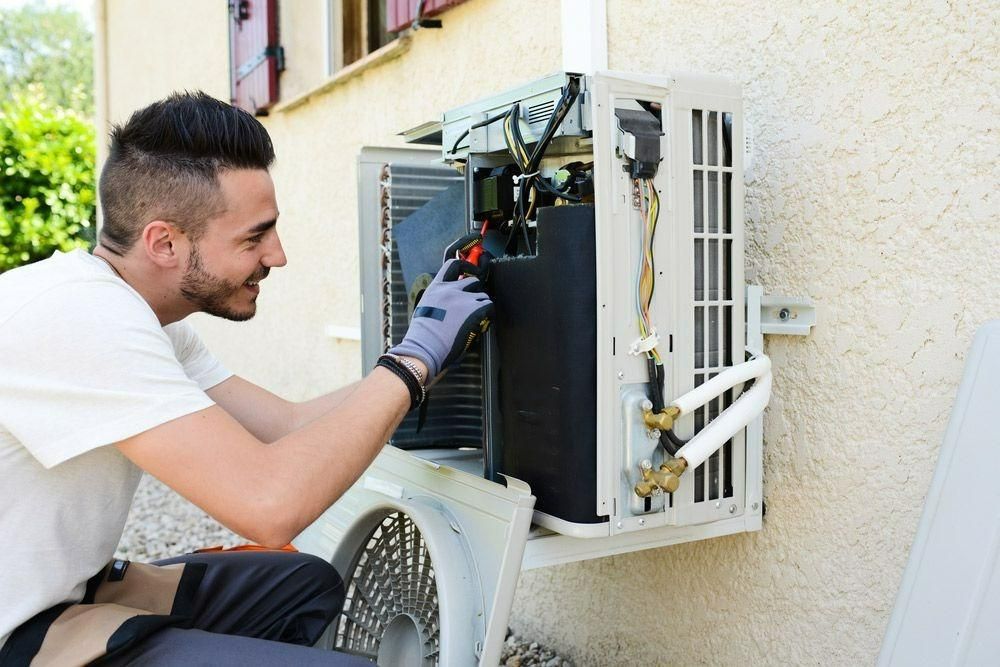 A Man Is Fixing An Air Conditioner On The Side Of A Building — Jervis Bay Airconditioning In Huskisson, NSW