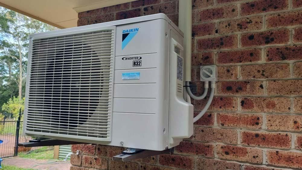 A White Air Conditioner Is Mounted On A Brick Wall — Jervis Bay Airconditioning In Huskisson, NSW