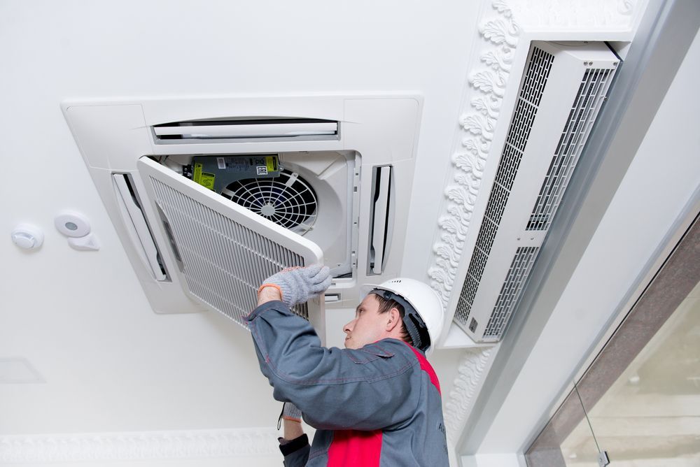 A technician installing a ceiling-mounted air conditioning unit