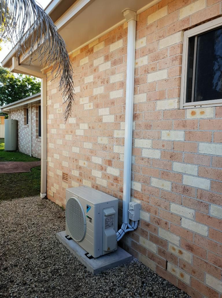 An Air Conditioner Is Sitting On The Side Of A Brick House — Jervis Bay Airconditioning In Sanctuary Point, NSW