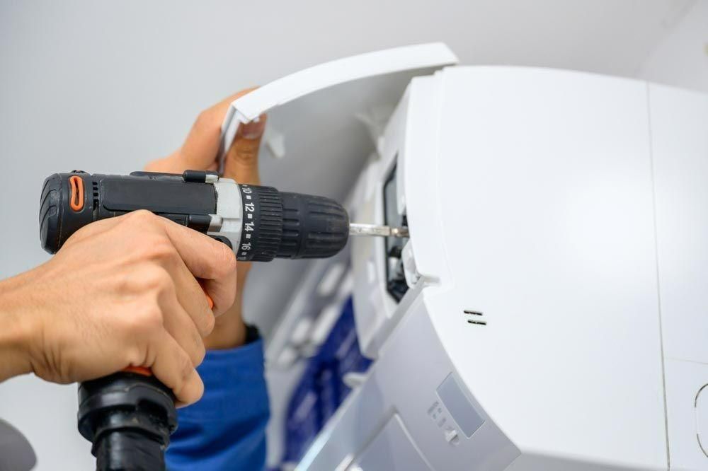 A Person Is Using A Drill To Fix An Air Conditioner — Jervis Bay Airconditioning In Huskisson, NSW