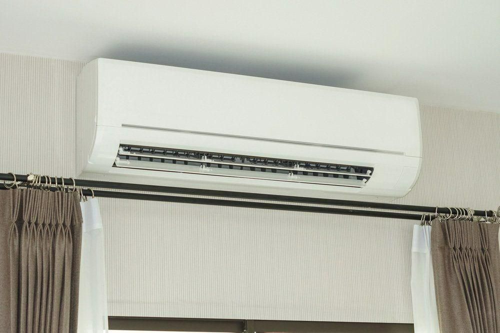 A White Air Conditioner Is Mounted To The Ceiling Above A Window — Jervis Bay Airconditioning In Huskisson, NSW